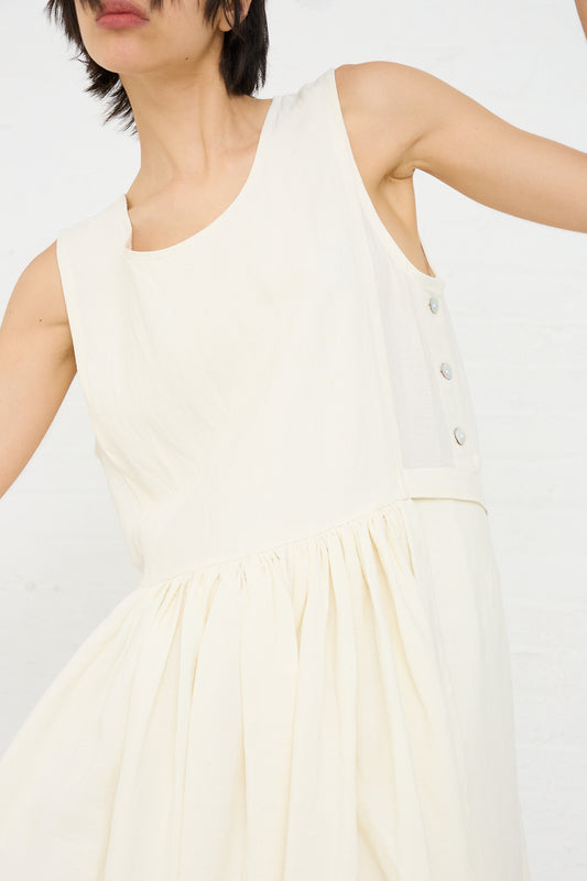 A person in a Cawley Irish Linen Apron Dress in Ecru with button details is shown from the shoulder down to mid-thigh against a white background.