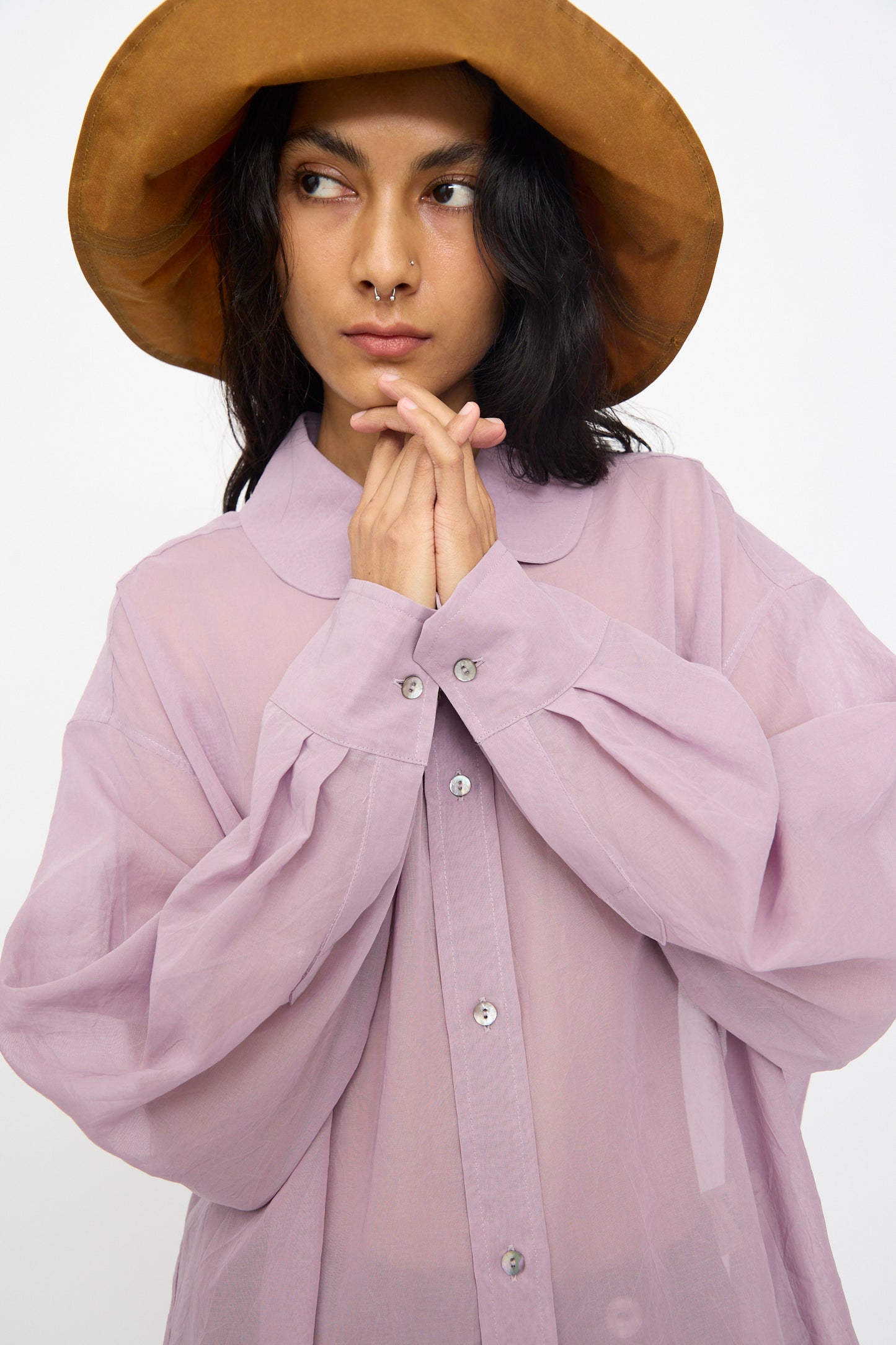 A person wears the Cawley Japanese Cotton Dyed Voile Phoebe Shirt in Purple, standing against a plain white background with hands clasped near their face.