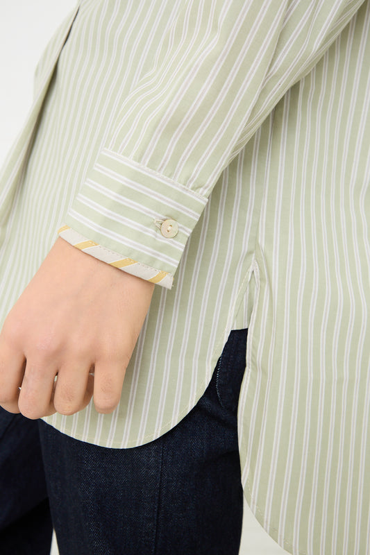 Close-up of a person wearing a Cawley Japanese Cotton Ines Shirt in Mint and Ecru with the cuff unbuttoned, paired with dark blue jeans.