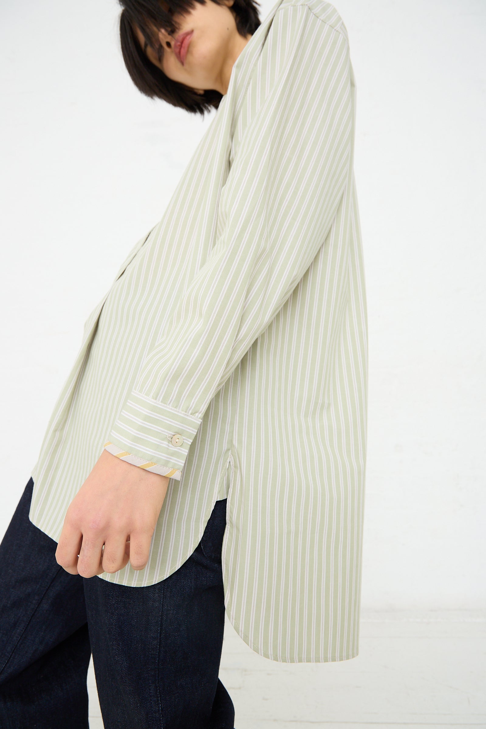 A person in a Japanese Cotton Ines Shirt in Mint and Ecru by Cawley, reflecting British manufacturing, and blue jeans with their head tilted downward, obscuring their face from view.