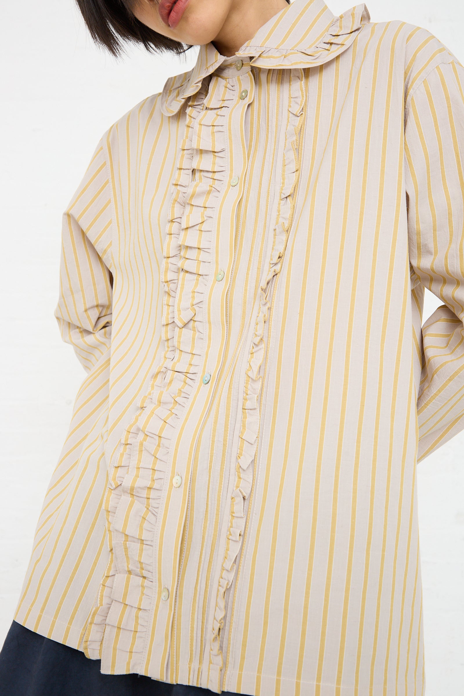 A close-up view of a person wearing a Cawley Japanese Cotton Ruffle Shirt in Sun and Grey with ruffles down the front.