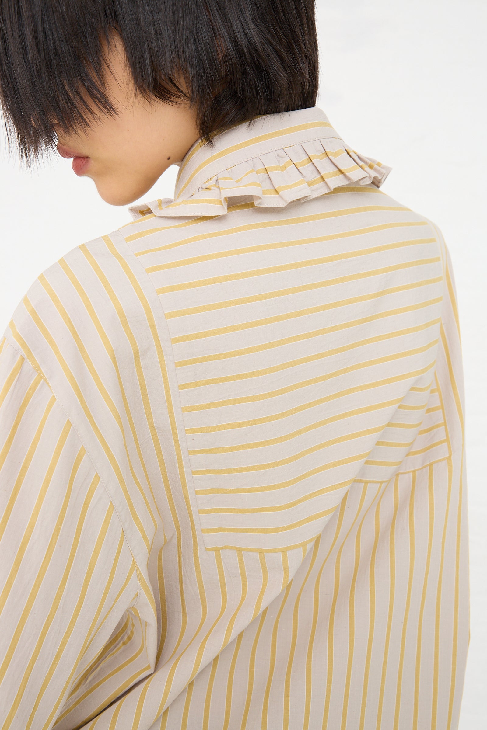 A person with short hair wearing a Cawley Japanese Cotton Ruffle Shirt in Sun and Grey with a focus on the ruffle collar and back.