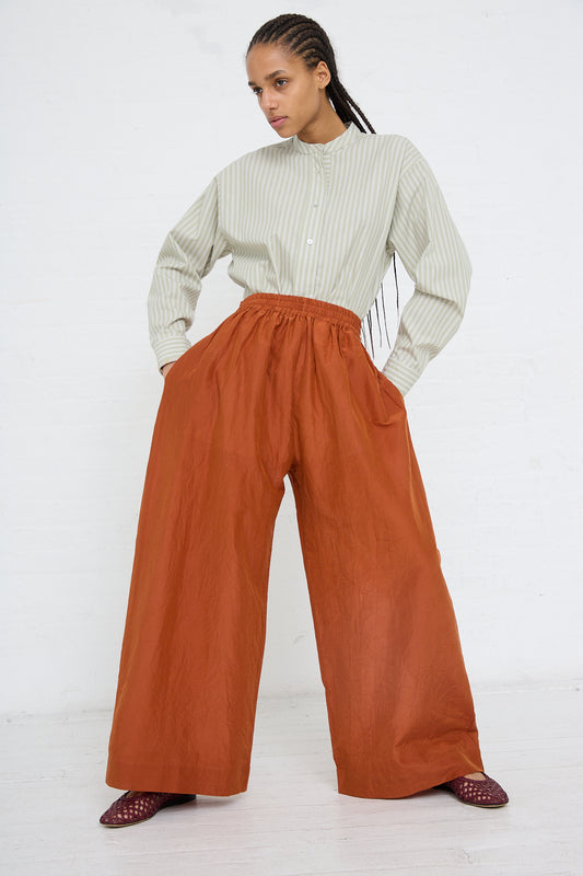 A woman in a striped shirt and Japanese Cotton Silk May Trouser Long in Rust by Cawley, boasting an elasticated waistband, stands against a white background.
