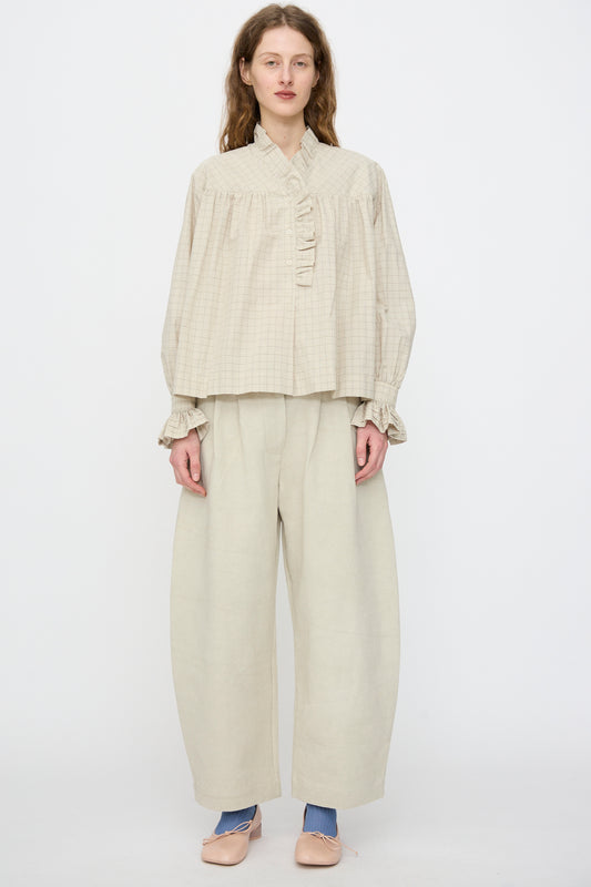 A woman faces forward wearing the Cawley Japanese Cotton Sophie Shirt in Natural Check, styled with wide light pleated pants, blue socks, and light pink shoes.
