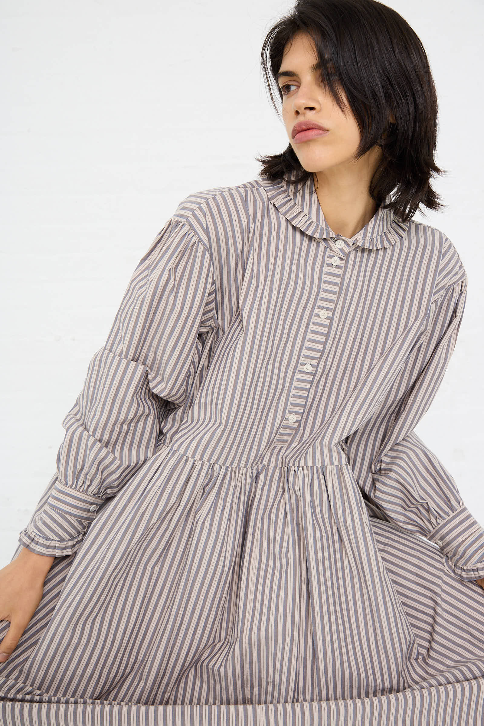 Person wearing the Lydbrook Dress in Natural, Blue, and Brown Stripe by Cawley, seated against a plain white background.