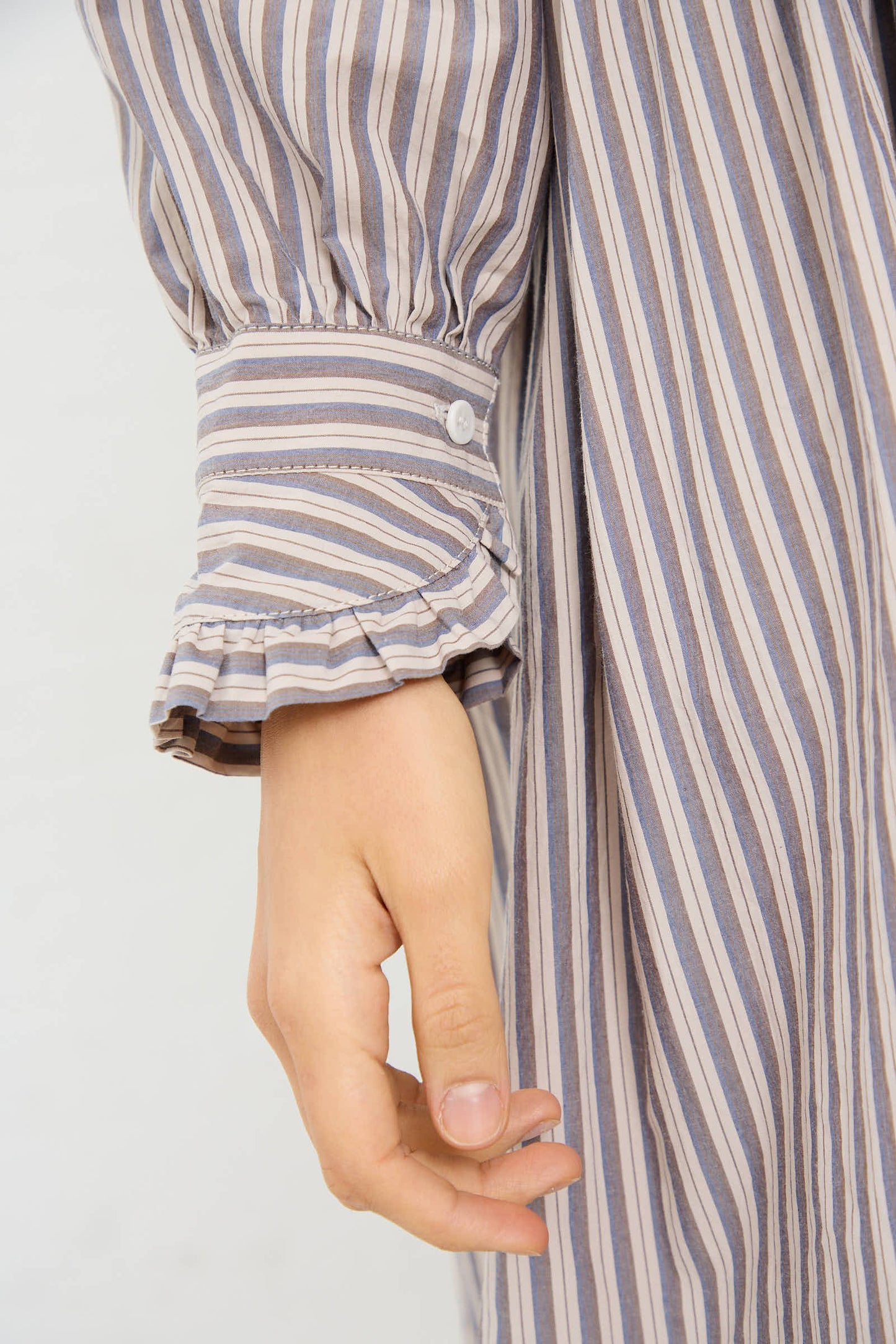 Close-up of a hand beside the Japanese striped cotton fabric of the Lydbrook Dress in Natural, Blue and Brown Stripe by Cawley, featuring a ruffled cuff with button details.