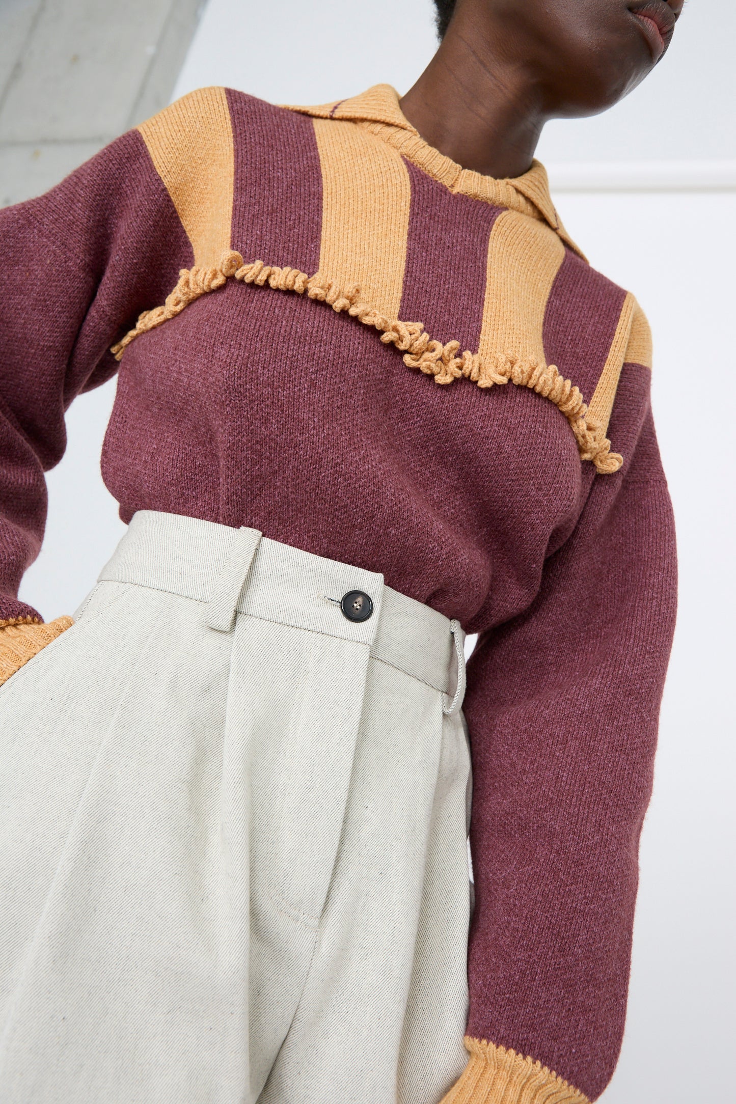 A person wearing a maroon and yellow striped sweater with ruffle details with Cawley's Japanese Denim Mara Jean in Ecru and Black, viewed from below. 