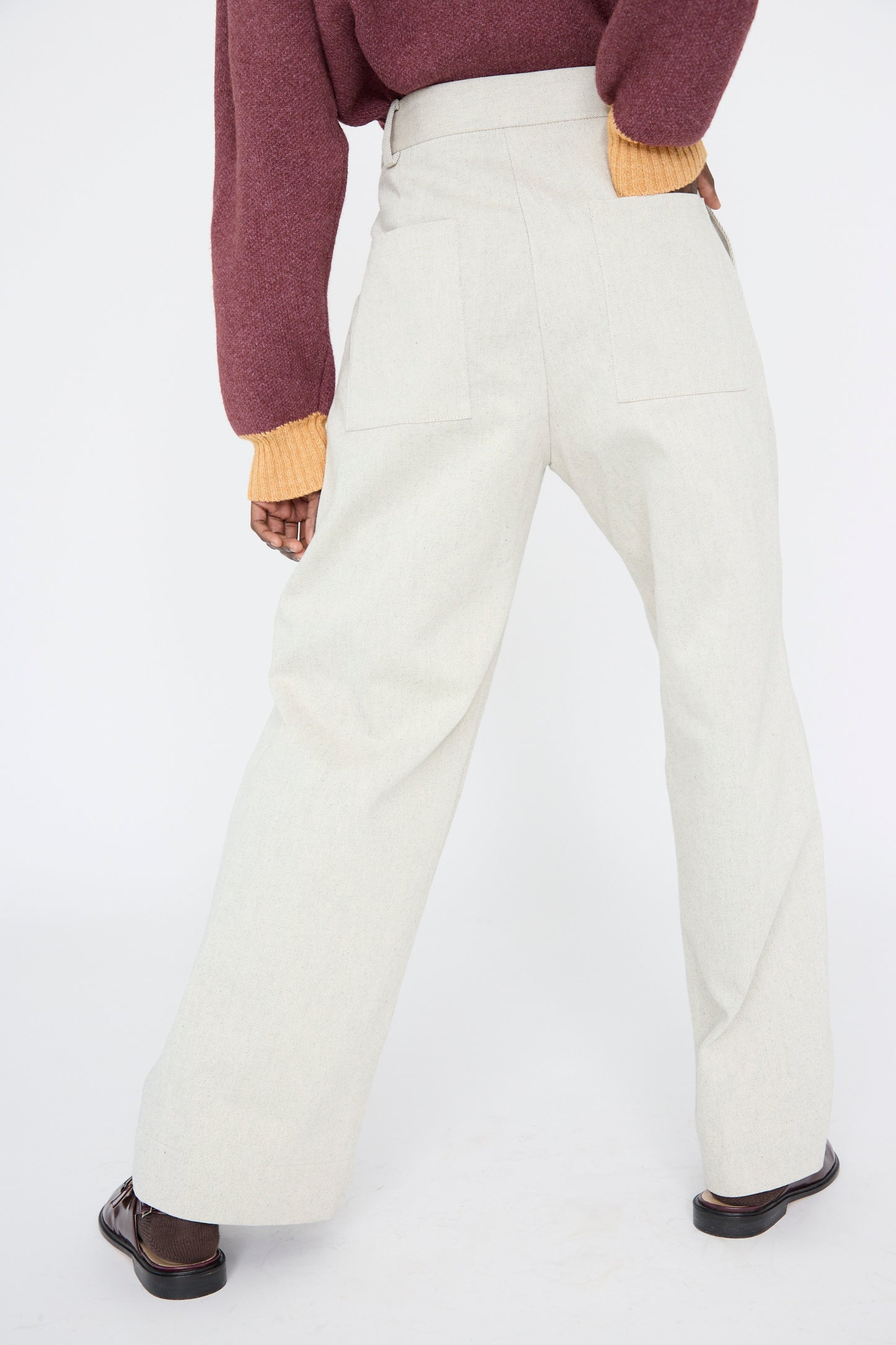 The model stands with their back to the camera, wearing a maroon sweater with yellow cuffs and Cawley's Japanese Denim Mara Jean in Ecru and Black.