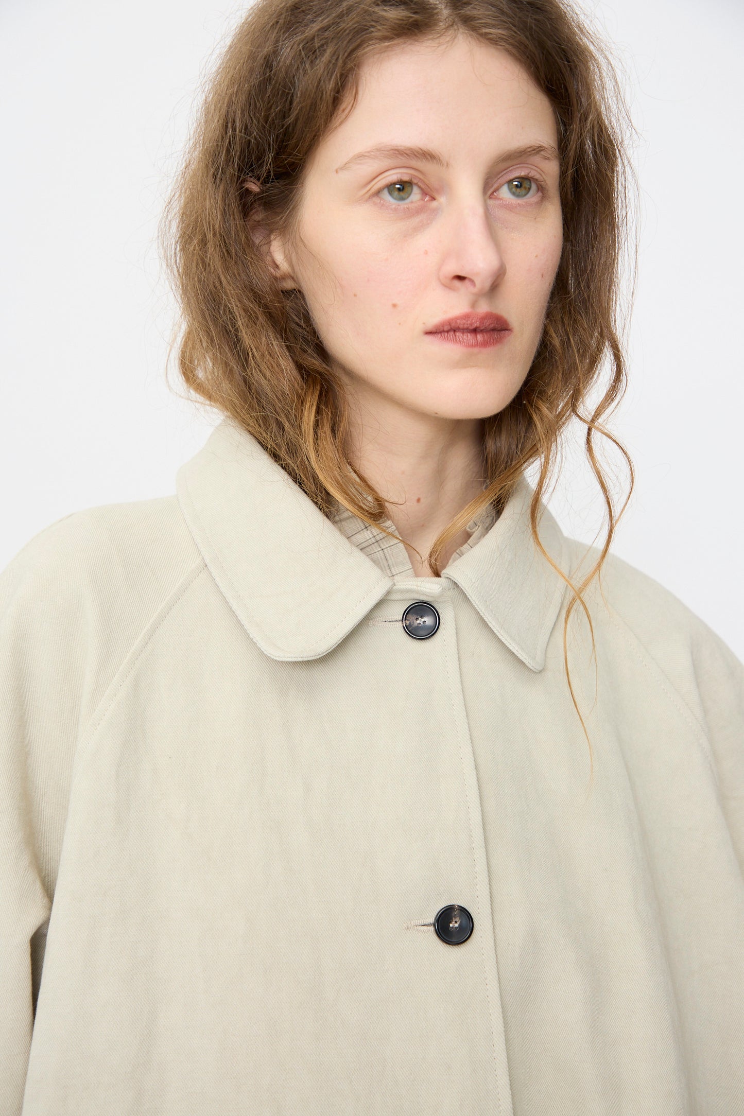 A person with long wavy hair wears the Cawley Japanese Drill Wickham Mac in Natural, standing against a plain light background.
