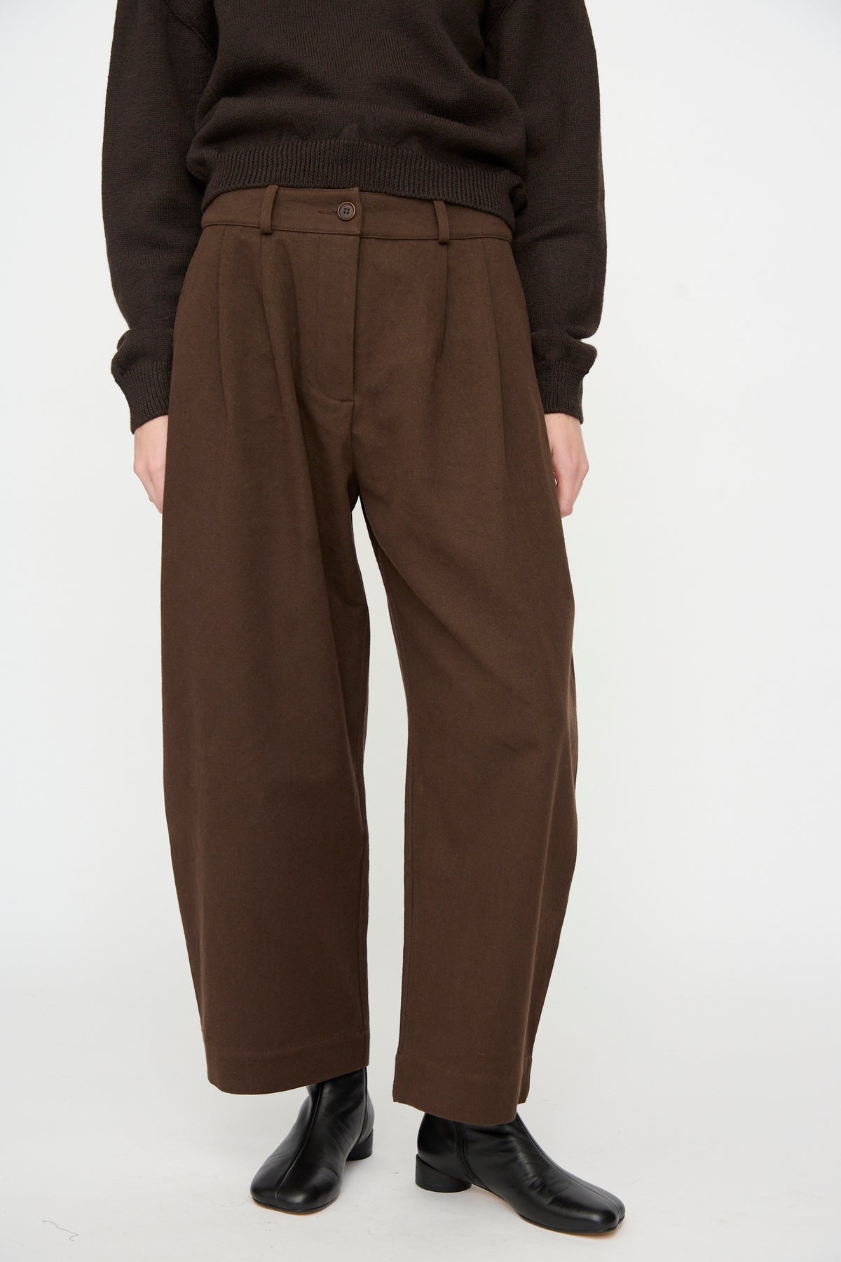 A person wears the Cawley Japanese Gabardine Robyn Trouser in Espresso with black ankle boots and a brown long-sleeve top, standing against a plain white background.