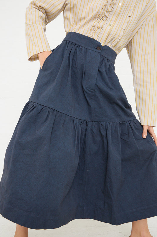 A person is shown from the waist down, wearing a striped yellow shirt tucked into a Cawley Japanese Heavy Cotton Patience Big Gathered Skirt in Dark Navy with a ruffled hemline.
