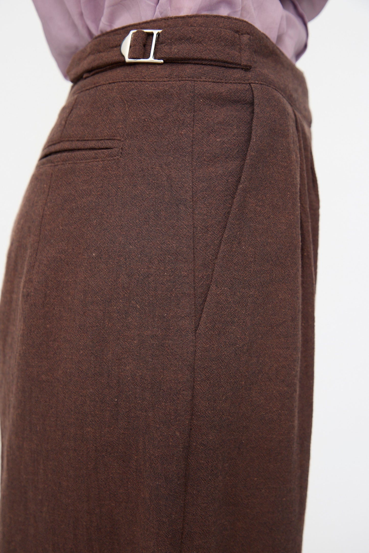 Close-up of a person wearing Cawley’s Japanese High Twisted Poplin Enya Trouser in Fog Purple, featuring an adjustable waistband and back pocket, paired with a light purple tucked-in shirt.
