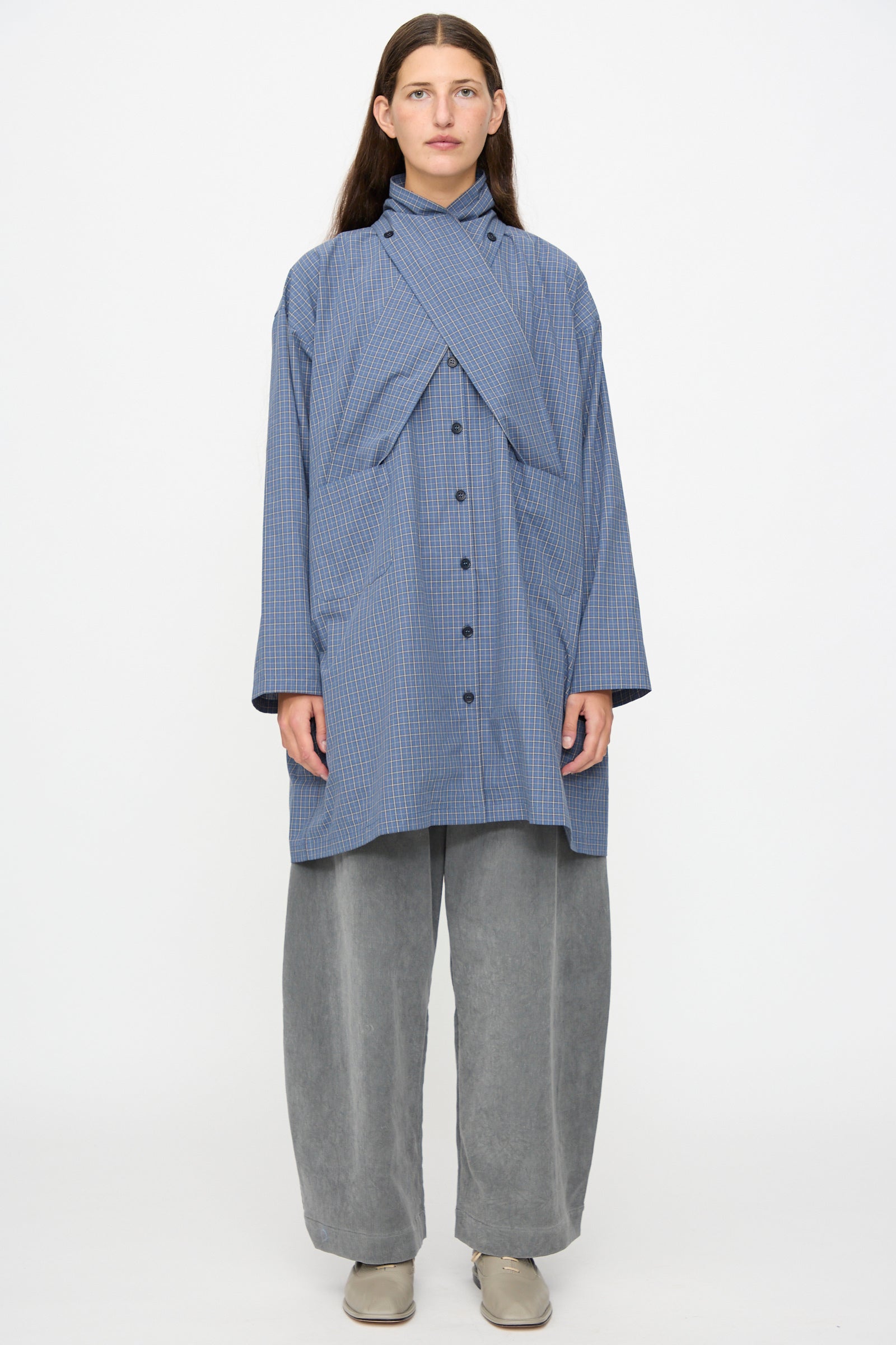 A person stands against a white background wearing the Cawley Japanese Mini Check Cotton Dorothy Dress in Blue.