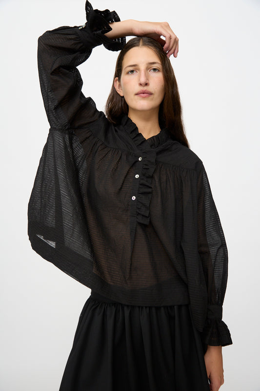A person with long brown hair wears the Cawley Japanese Sheer Stripe Cotton Sophie Shirt in Midnight, styled with a black skirt, and poses with one arm raised above their head against a plain white background.