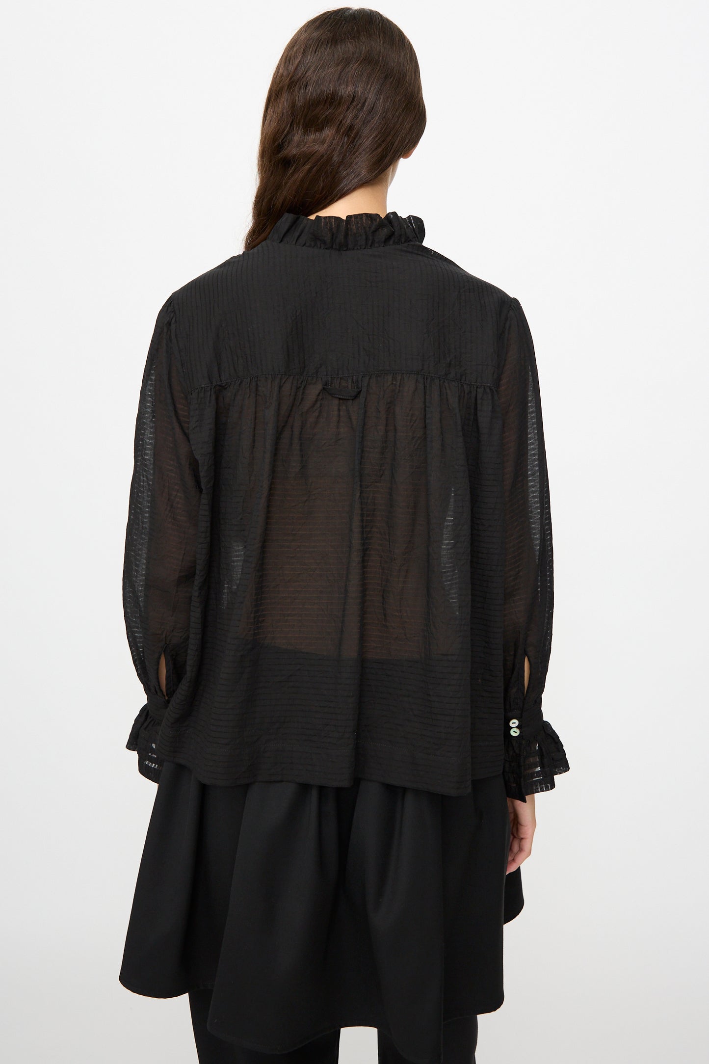 A person with long brown hair is seen from the back, wearing the Cawley Japanese Sheer Stripe Cotton Sophie Shirt in Midnight and a layered black skirt.
