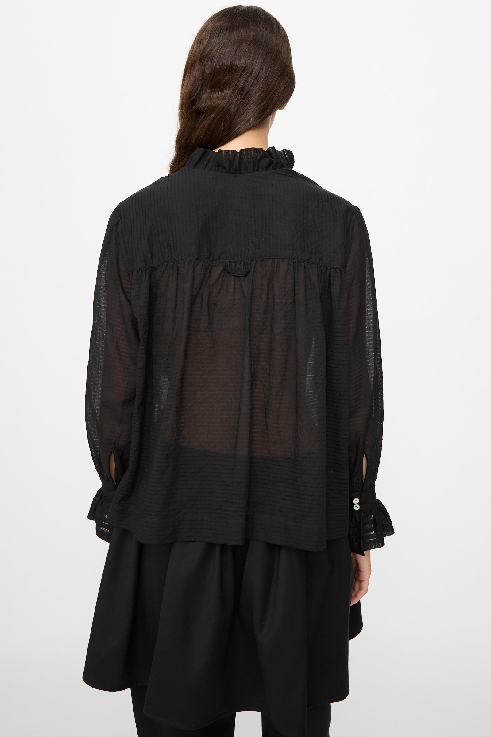A person with long brown hair is seen from the back, wearing the Cawley Japanese Sheer Stripe Cotton Sophie Shirt in Midnight and a layered black skirt.