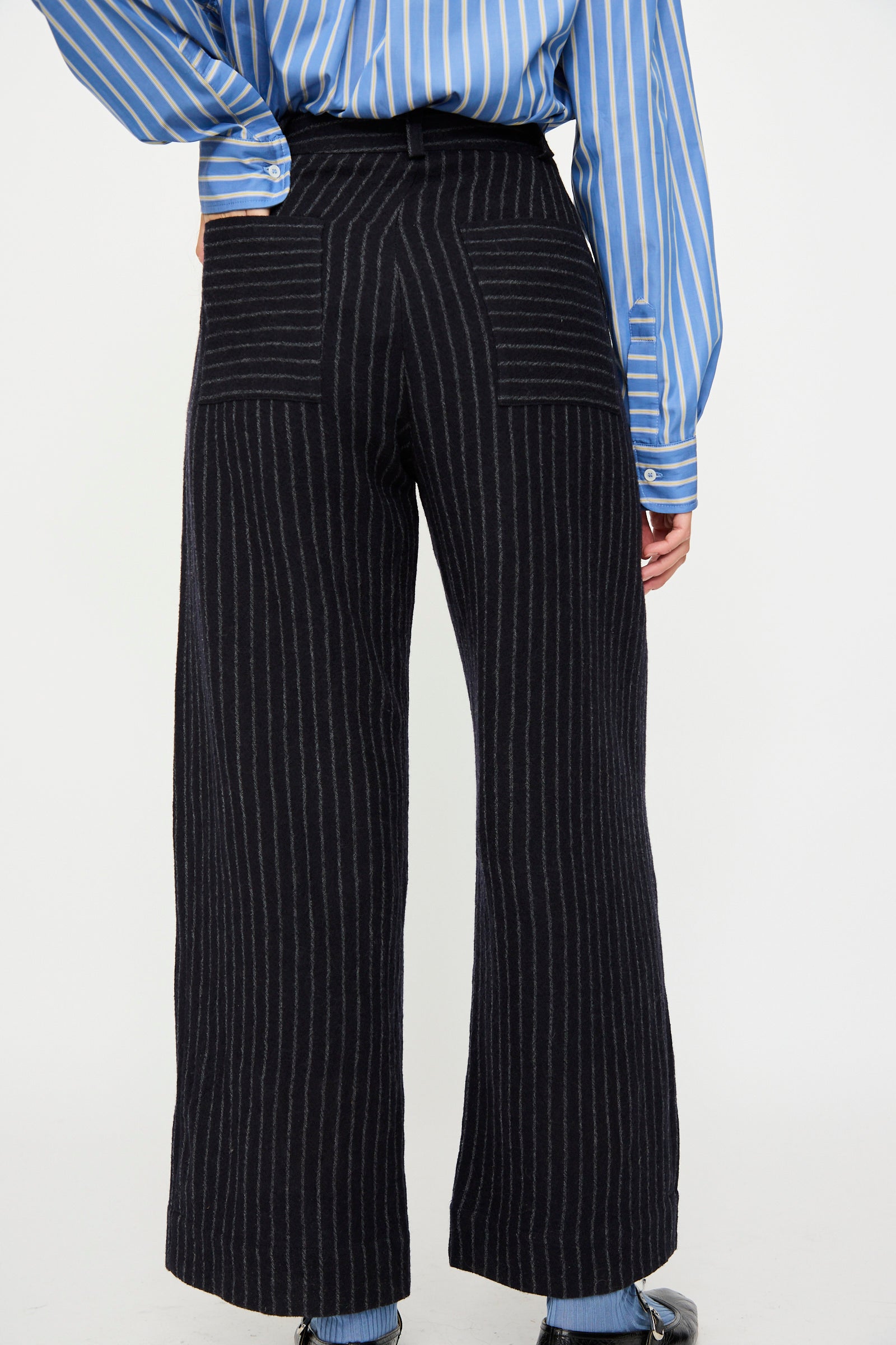 A person is seen from the back wearing Cawley’s Japanese Striped Boucle Mara Trouser in Navy and Grey, featuring modern wide legs and unique vertical and horizontal pinstripes for a chic London-made look.