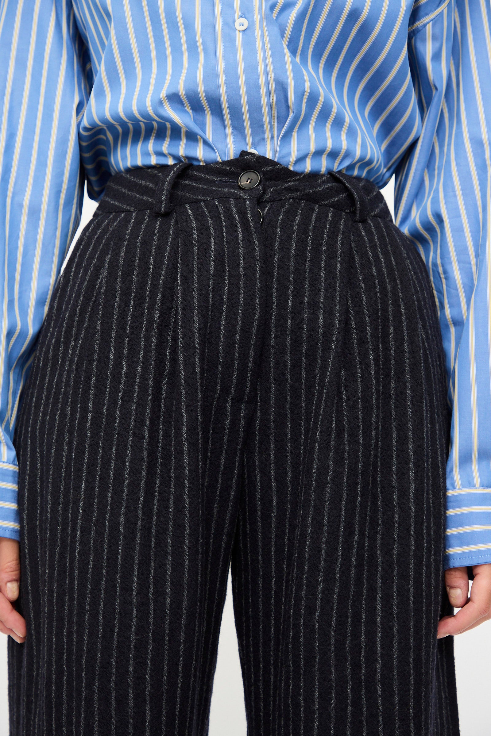 Person wearing a blue and white striped button-up shirt tucked into Cawley's Japanese Striped Boucle Mara Trouser in navy and grey.