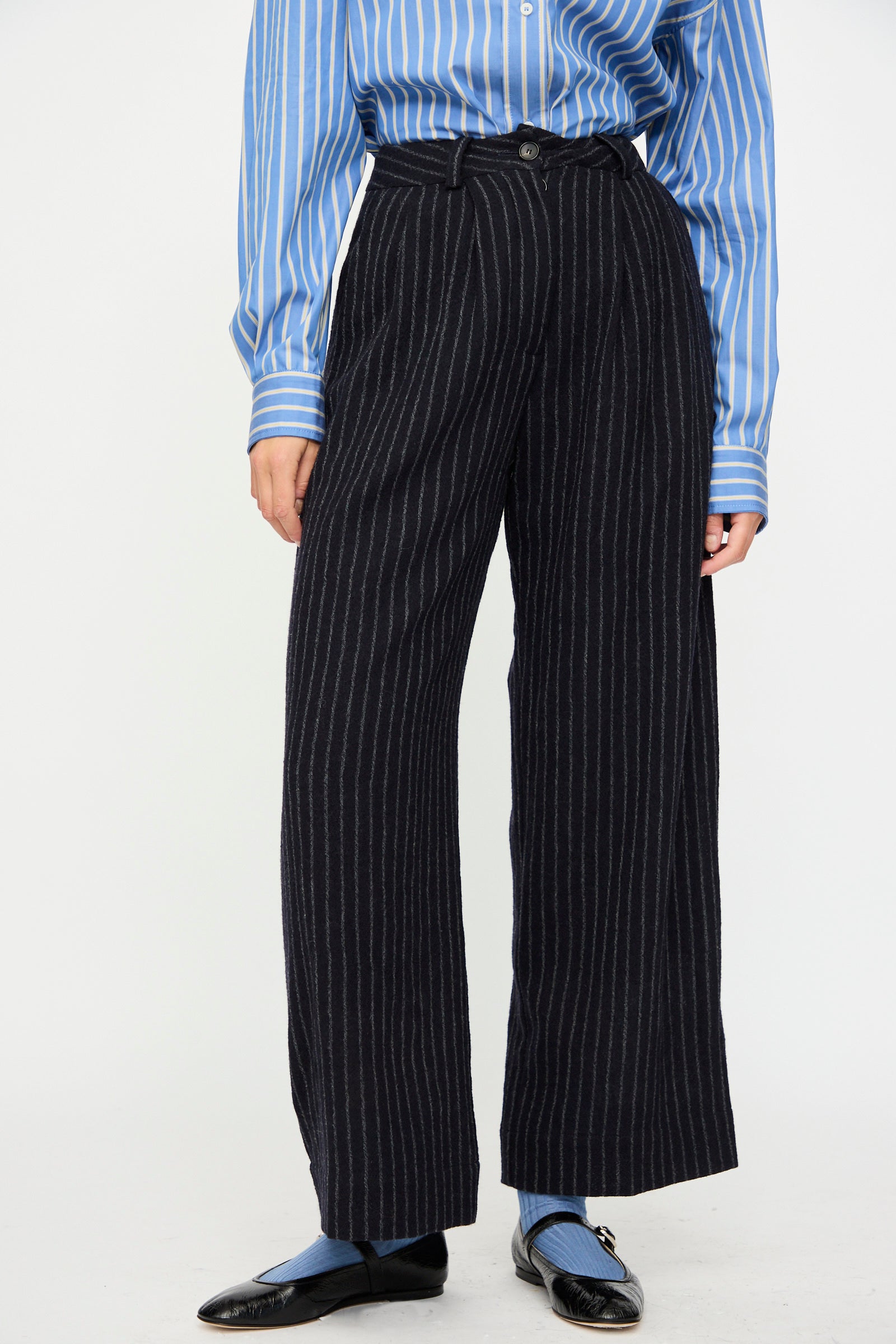 Person wearing a blue and white striped shirt, Cawley Japanese Striped Boucle Mara Trouser in Navy and Grey, blue socks, and black shoes, standing against a plain background.