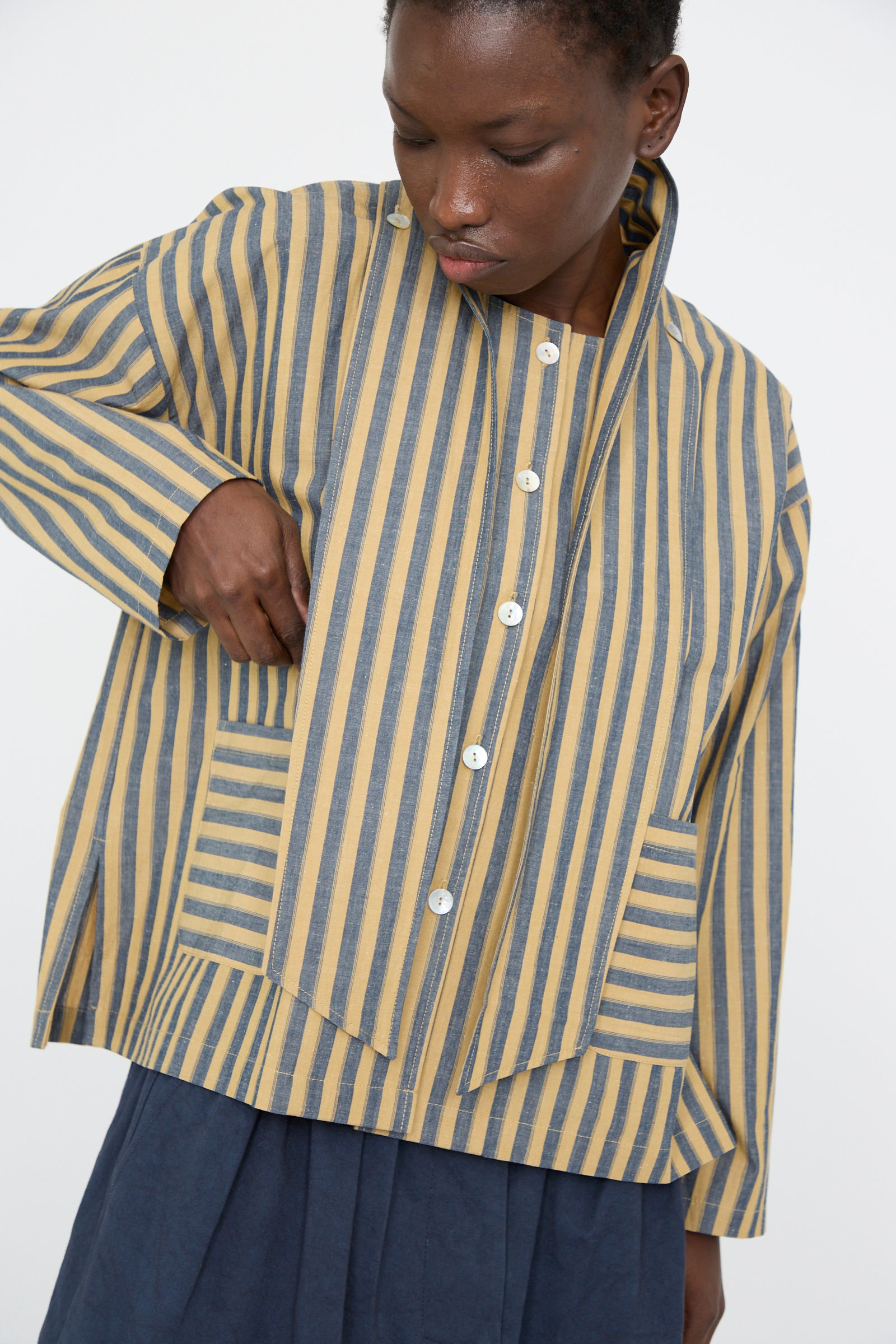 A person looking down is wearing the Cawley Japanese Striped Cotton Dorothy Shirt in mustard and navy, worn over a blue skirt against a plain background.