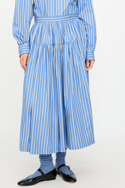 Person wearing a Cawley Japanese Striped Shirting Panel Skirt in Dandelion with a matching shirt, blue socks, and black shoes stands against a plain background. 
