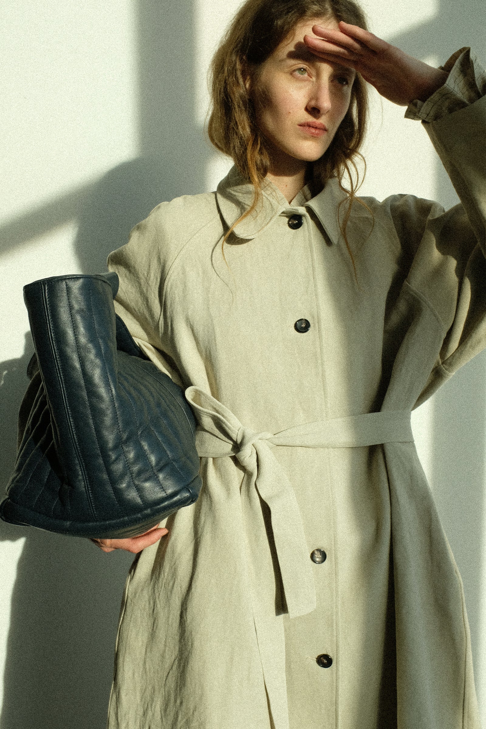 Woman in a Japanese Drill Wickham Mac in Natural holding Quilted Nappa Large Tote Bag with Coin Purse in Navy against a white wall.