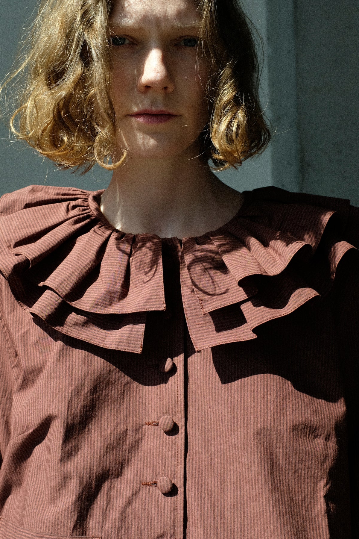 A cropped image of a woman wearing Cawley's Japanese Typewriter Cotton Rowan Jacket in Burgundy Stripe in the sunlight.