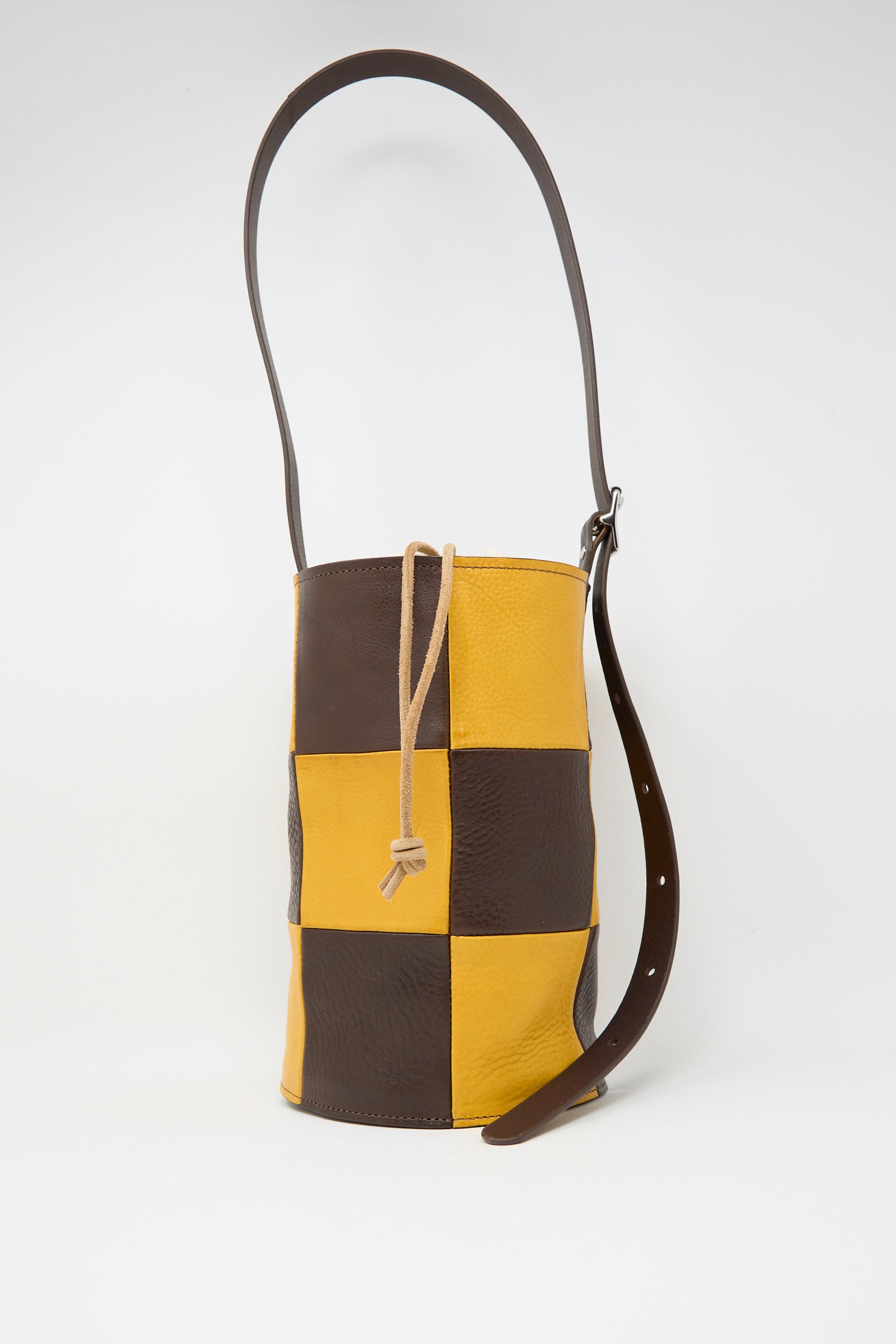 The Cawley Leather Patchwork Bucket Bag in Tan and Mustard features a checkered pattern and an adjustable strap for versatile wear.