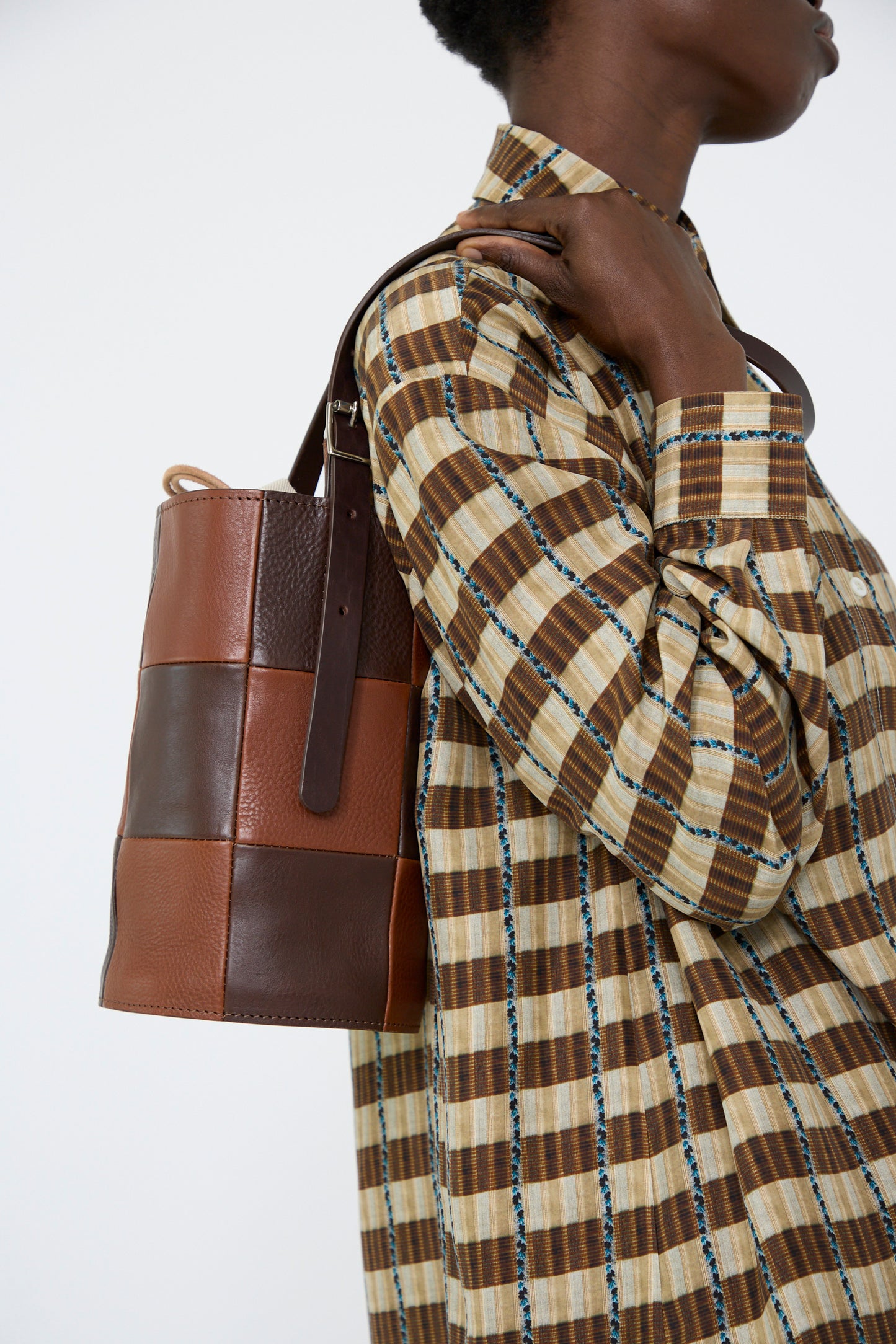 A person carrying the Leather Bucket Bag in Chocolate and Tan from Cawley,  paired with a brown plaid shirt, looking to the right.