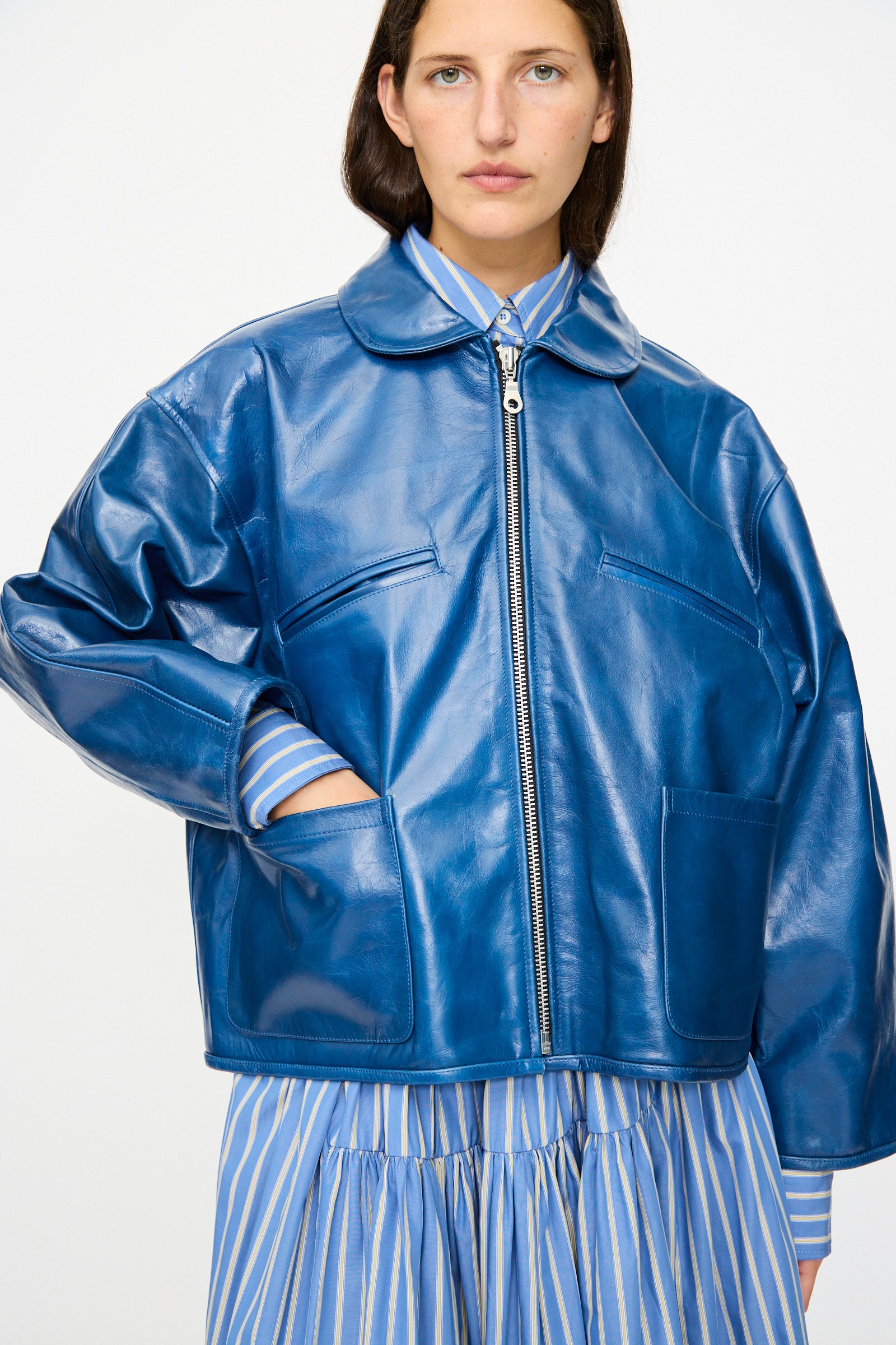 A person wears the Cawley Leather Flying Jacket in Canada Blue, styled with a blue and yellow striped shirt and skirt, standing against a plain background.