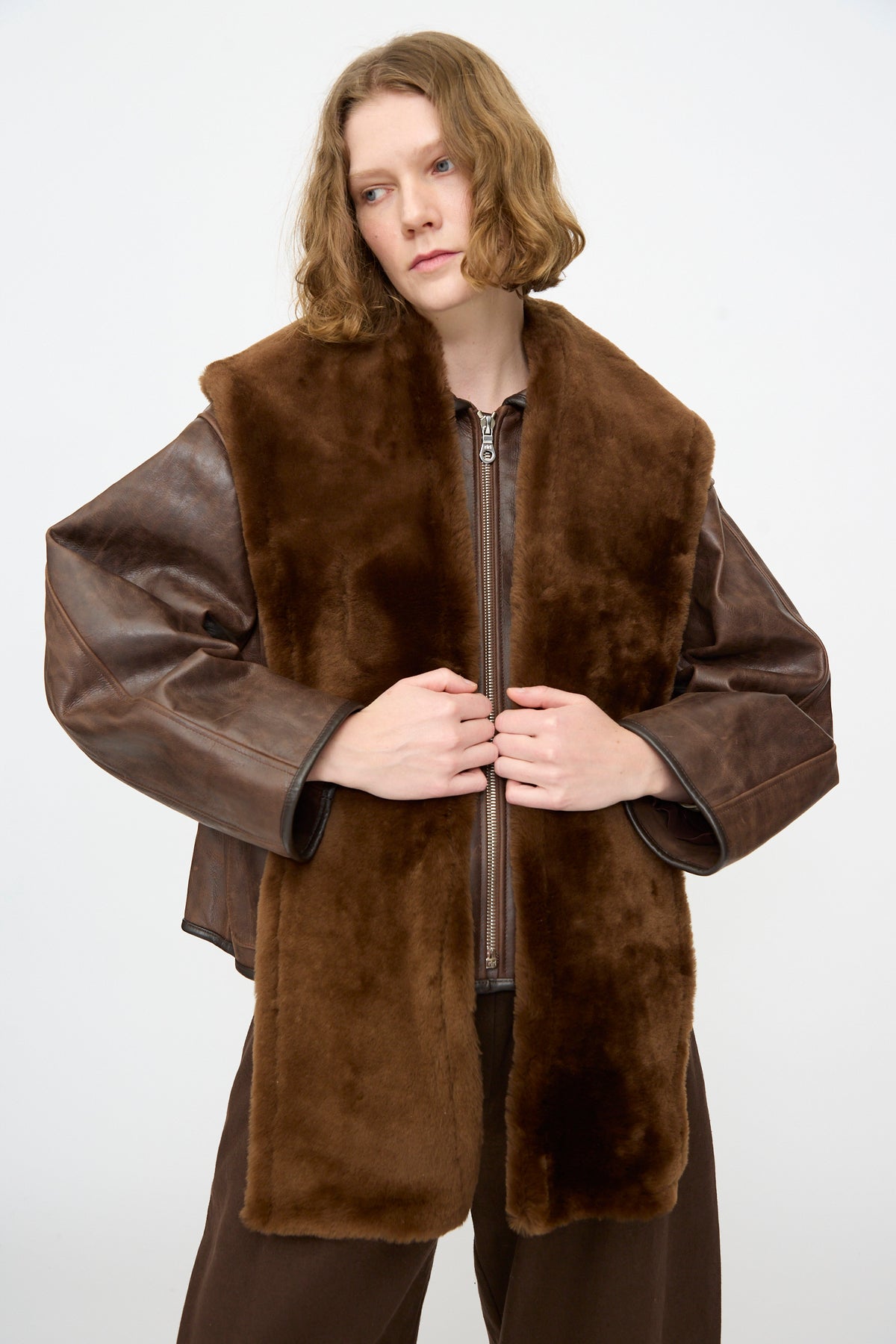 A person wearing the Cawley Leather Sheepskin Stole in Walnut, styled over a brown leather jacket, stands against a plain white background.