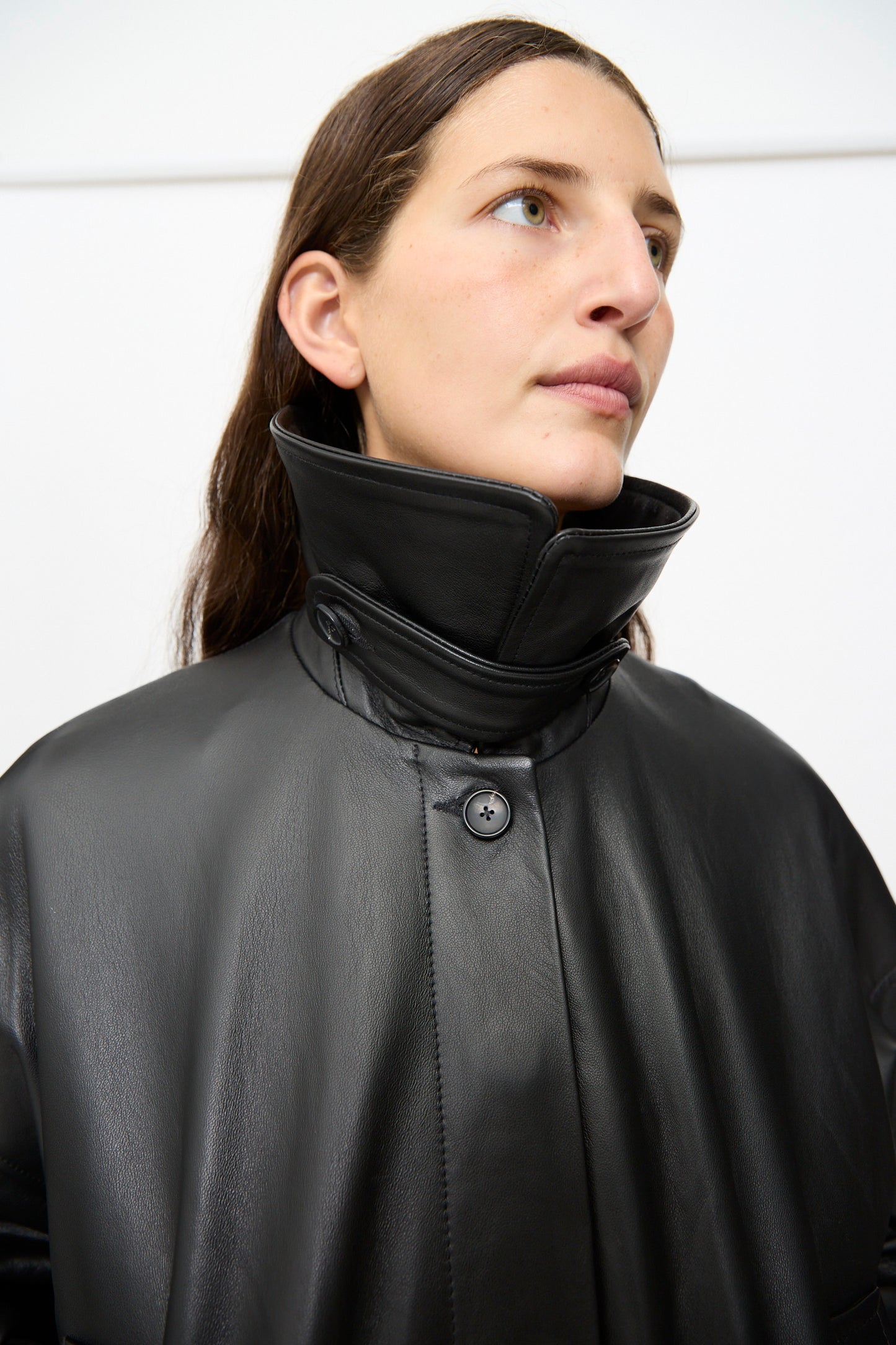 A person wearing the Cawley Nappa Leather Nara Jacket in Black, featuring an oversized fit and a high collar, looks slightly upward against a plain white background.