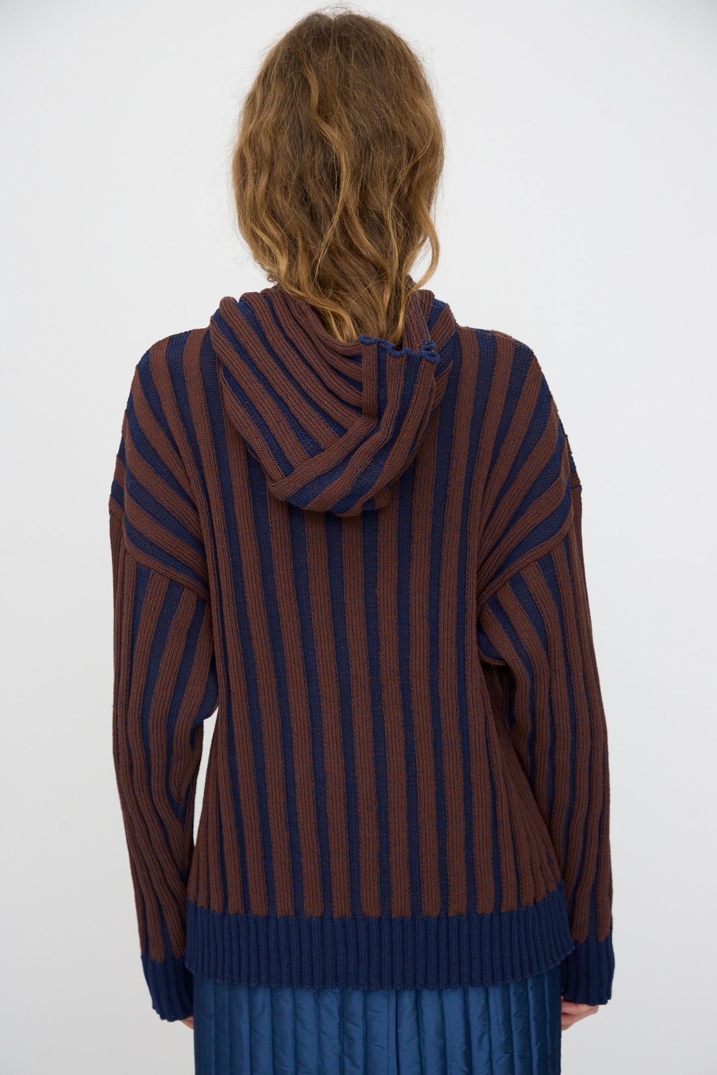 A person with wavy light brown hair is seen from the back wearing the Cawley Organic Cotton Zip Up Hoodie in Blu Kid and Choco.