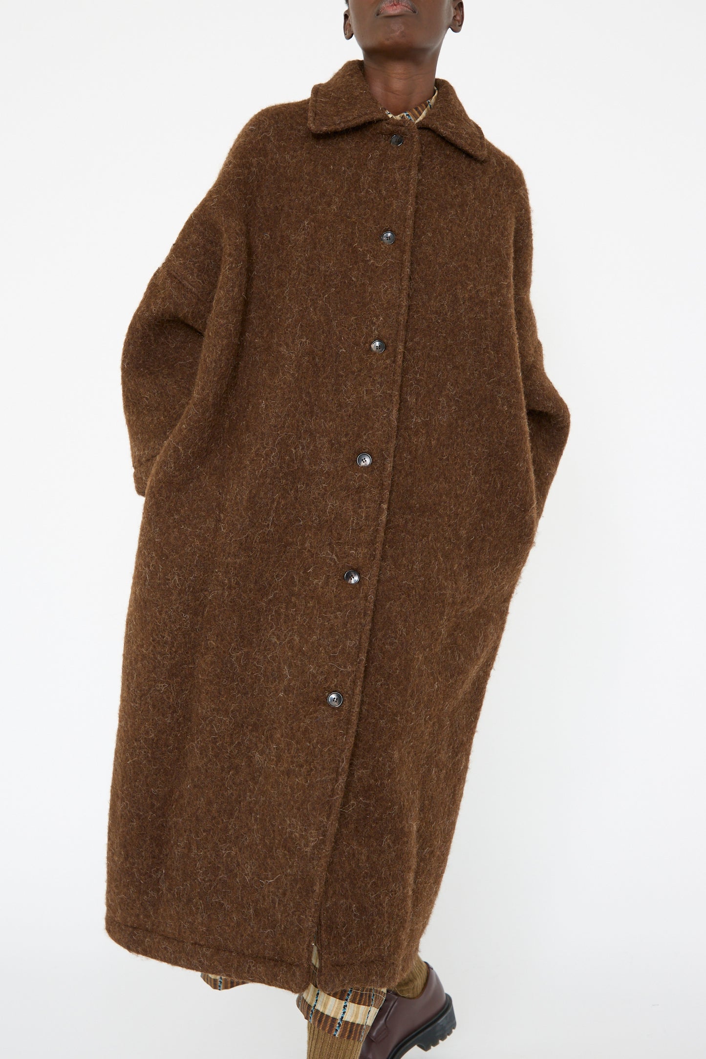 A person stands against a white background, wrapped in the Portuguese Long Hair Wool Faro Coat in Chocolate by Cawley, featuring buttons and an oversized fit.