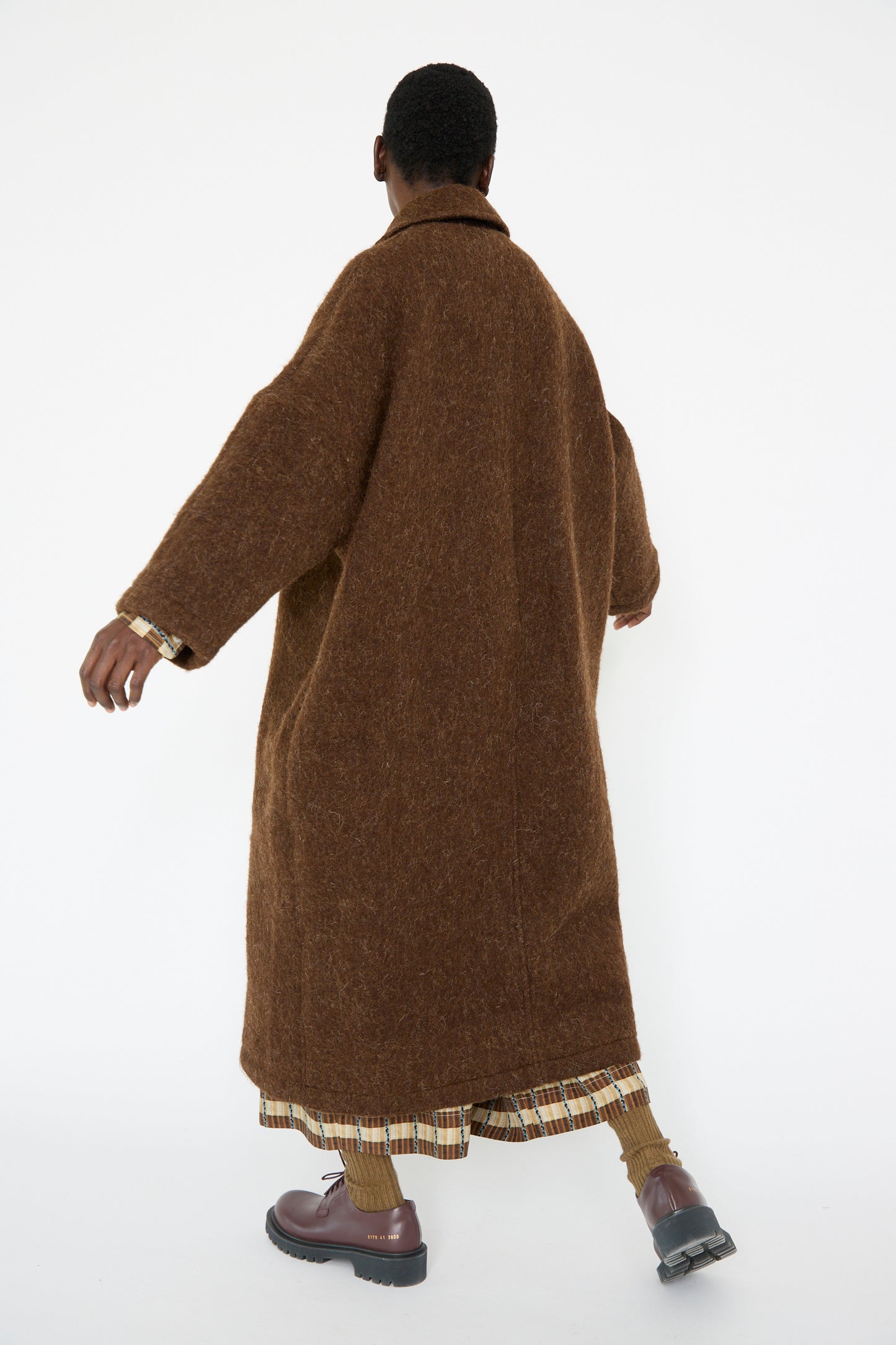 A person facing away wearing the oversized Portuguese Long Hair Wool Faro Coat in Chocolate by Cawley.