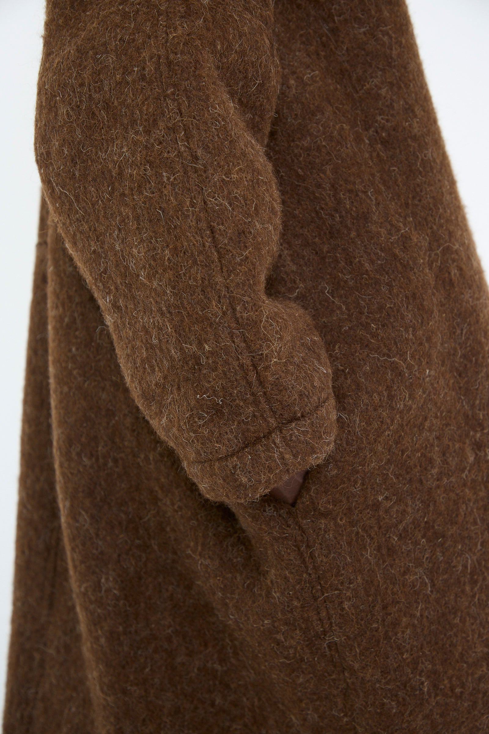 Close-up of a person wearing the Cawley Portuguese Long Hair Wool Faro Coat in Chocolate, highlighting the textured fabric and side pocket detail.