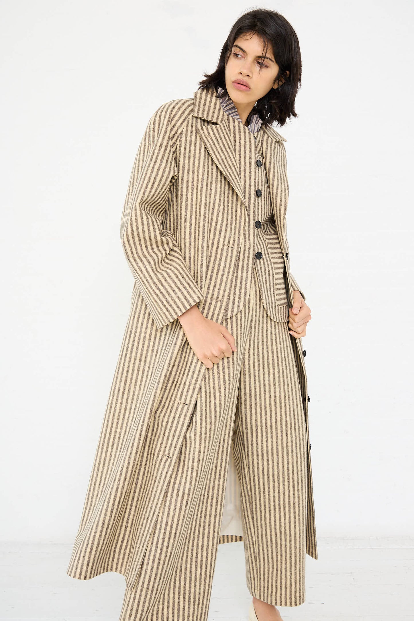 A person is wearing the Portuguese Striped Wool Annie Coat in Ecru and Brown by Cawley with matching wide-leg trousers, standing against a plain white background.