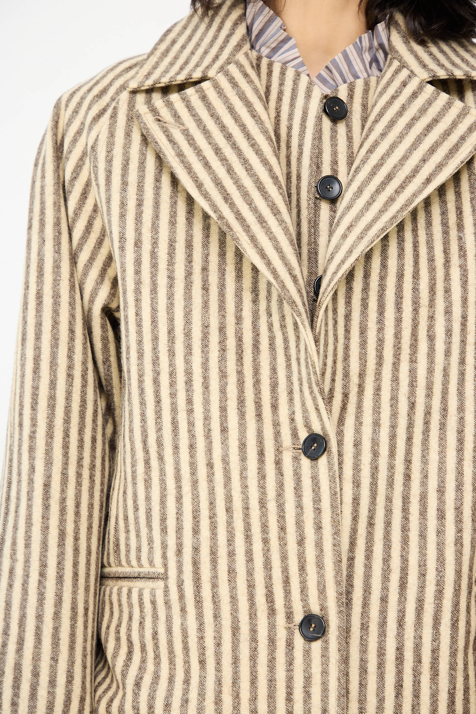 A close-up of a person wearing the Portuguese Striped Wool Annie Coat in Ecru and Brown by Cawley, featuring black buttons.