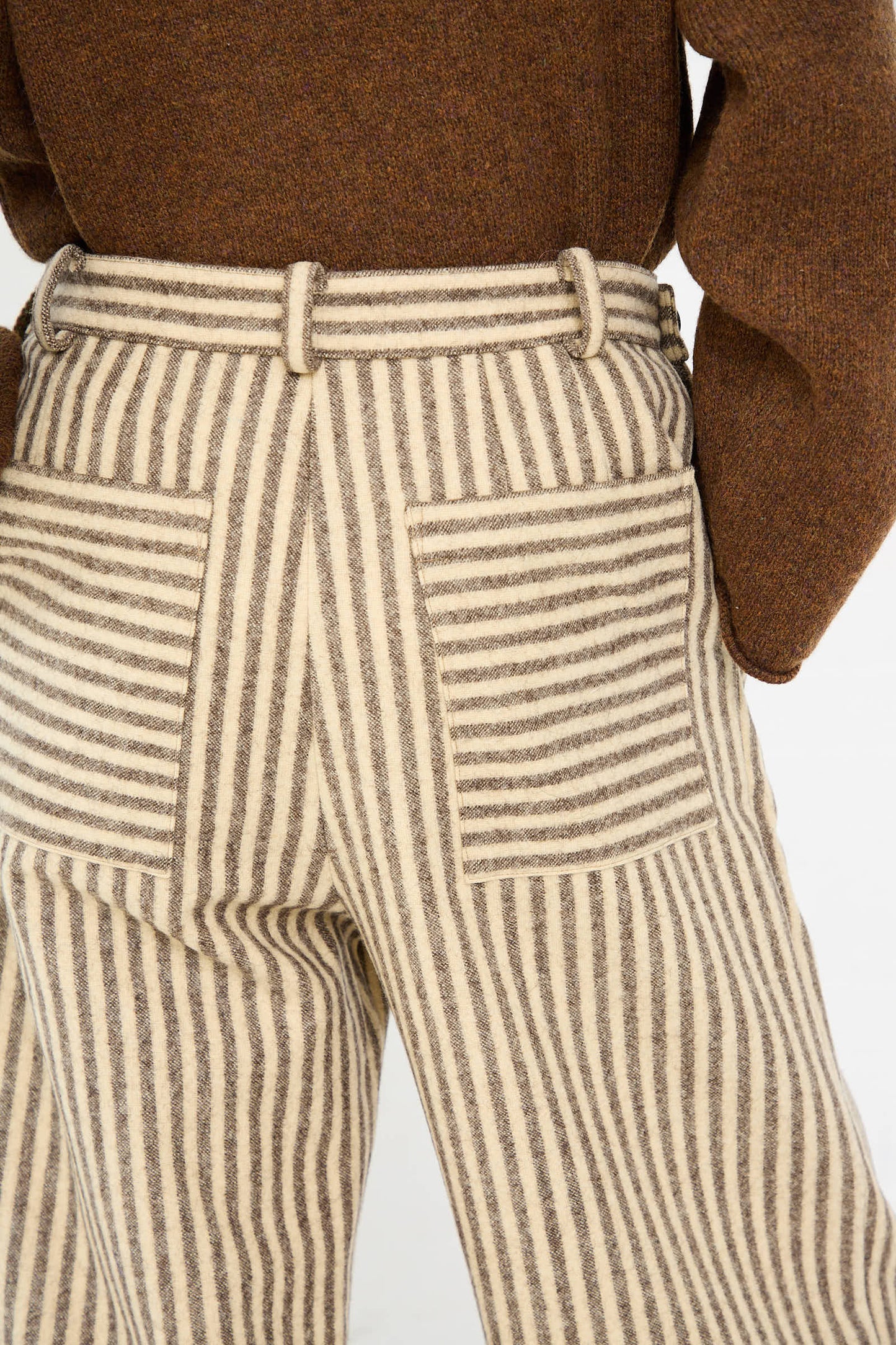 Person wearing a brown sweater and ecru and brown Portuguese Striped Wool Georgia Trouser by Cawley, with visible back pockets, taken from behind.