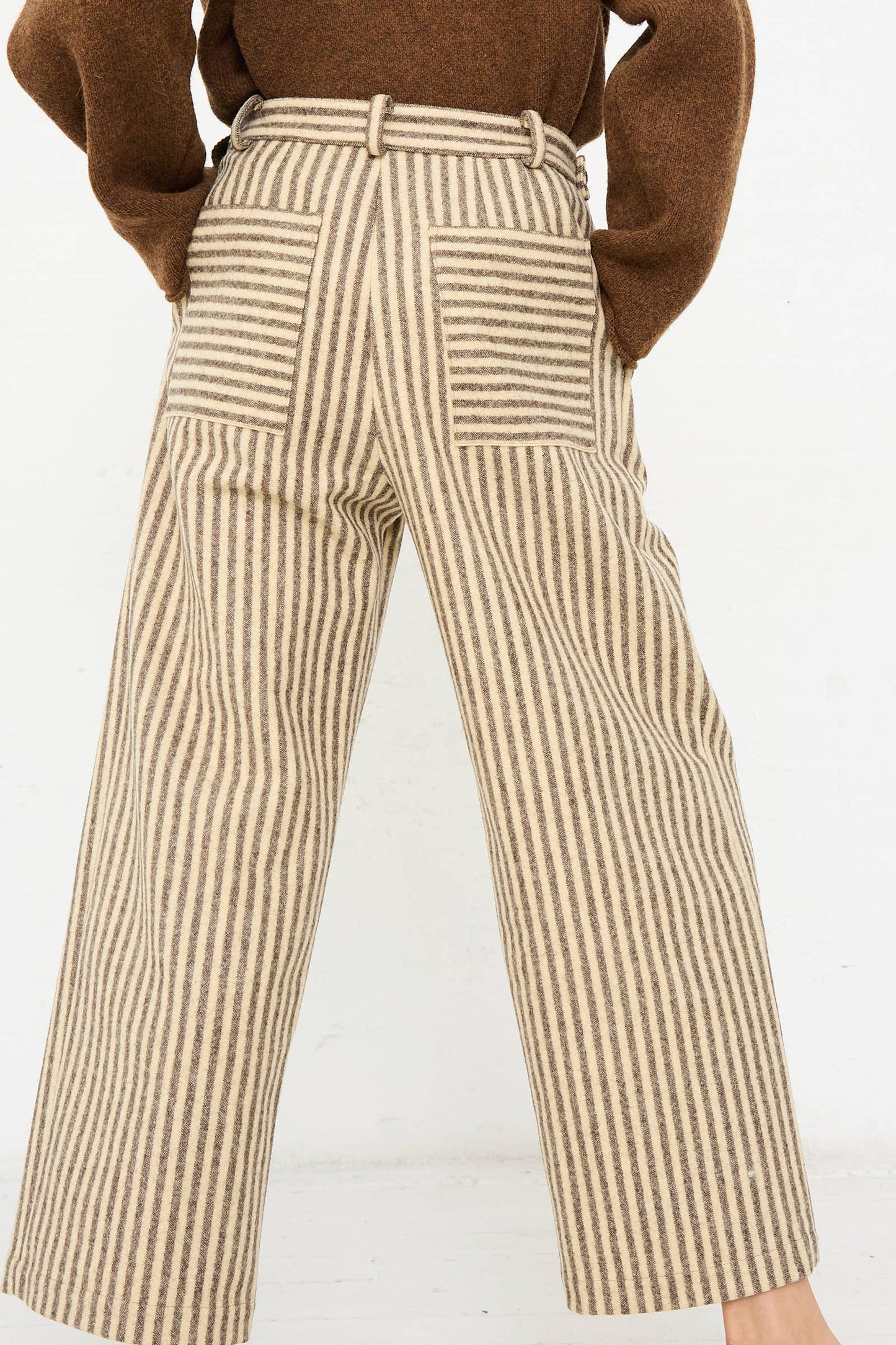 A person stands against a plain background, wearing the relaxed-fit, high-rise Portuguese Striped Wool Georgia Trouser in Ecru and Brown from Cawley, paired with a matching brown top.