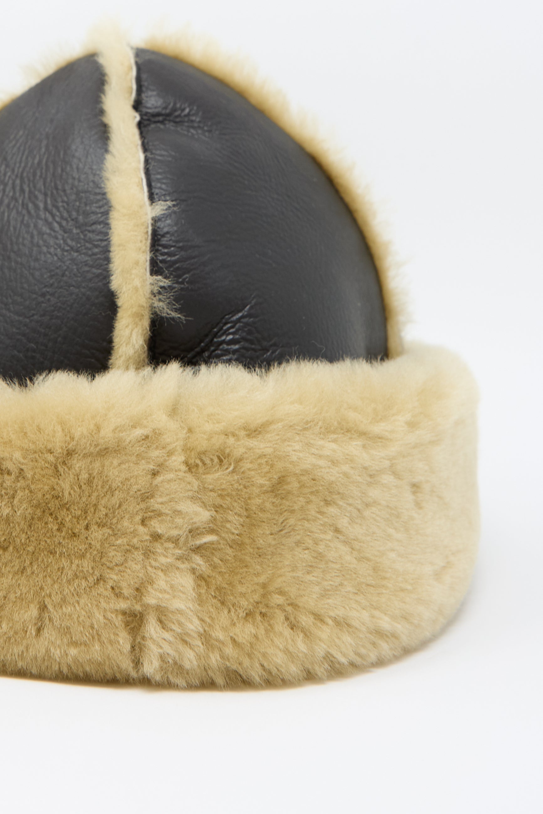 Close-up of the Sheepskin Leather Seam Hat by Cawley, featuring a fur-lined chocolate leather exterior with a tan fur trim, and intricate stitching on a white background.