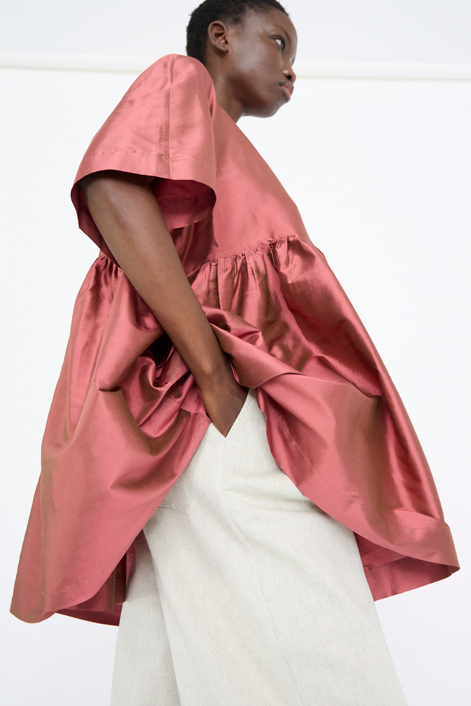 A person dressed in the Cawley Silk Dupion Delilah Dress in Rhubarb poses against a plain white background.