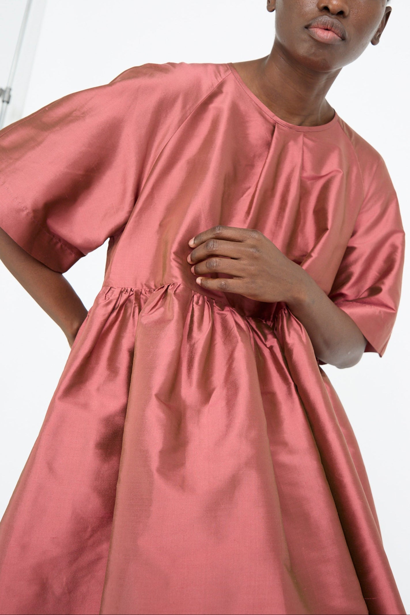 A person models the Cawley Silk Dupion Delilah Dress in rhubarb, featuring an oversized fit and crew neckline, set against a white background.