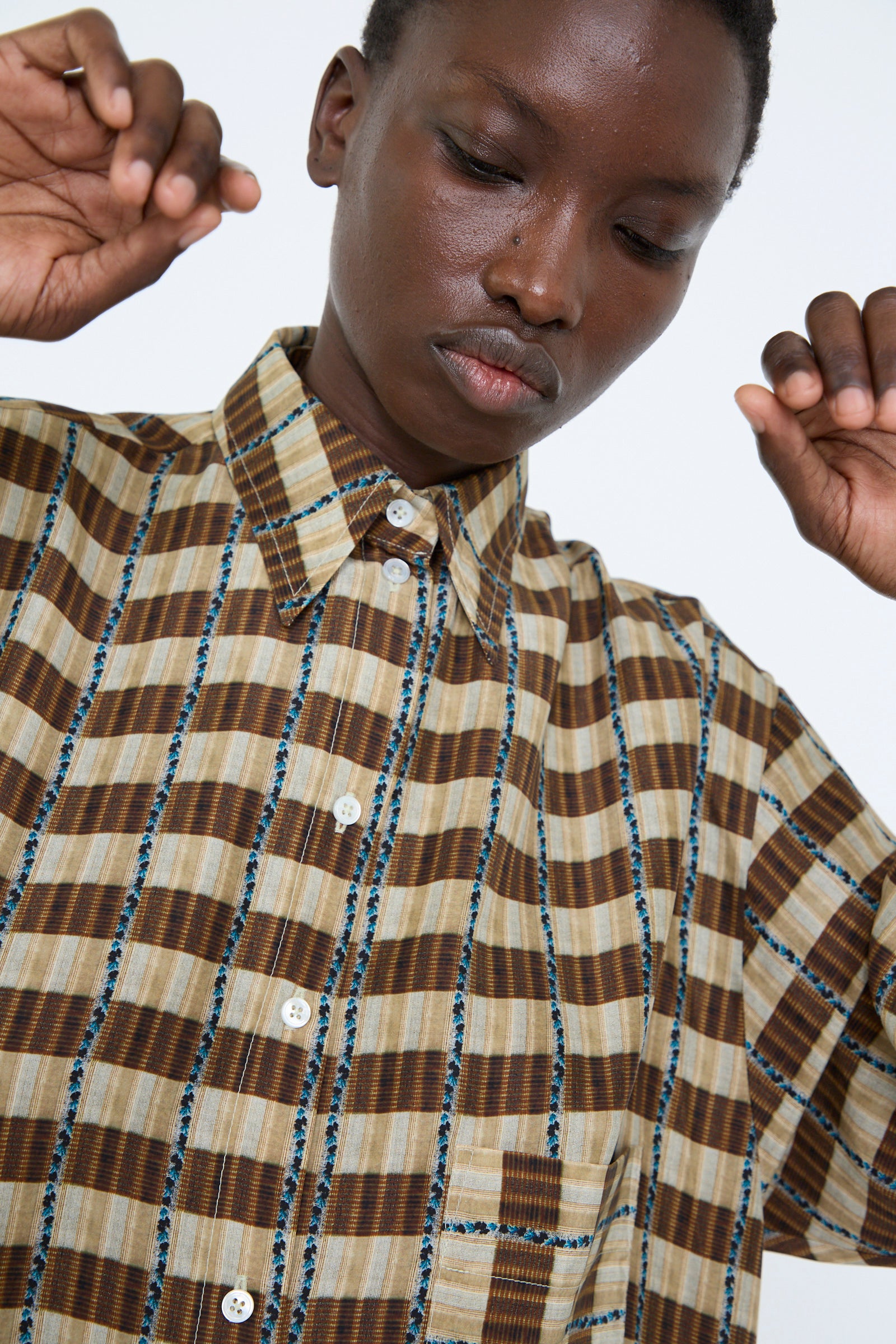 A close up of a person wearing Cawley's Silk Printed Big Shirt in Brown Plaid with corozo buttons raises their hands against a plain background.