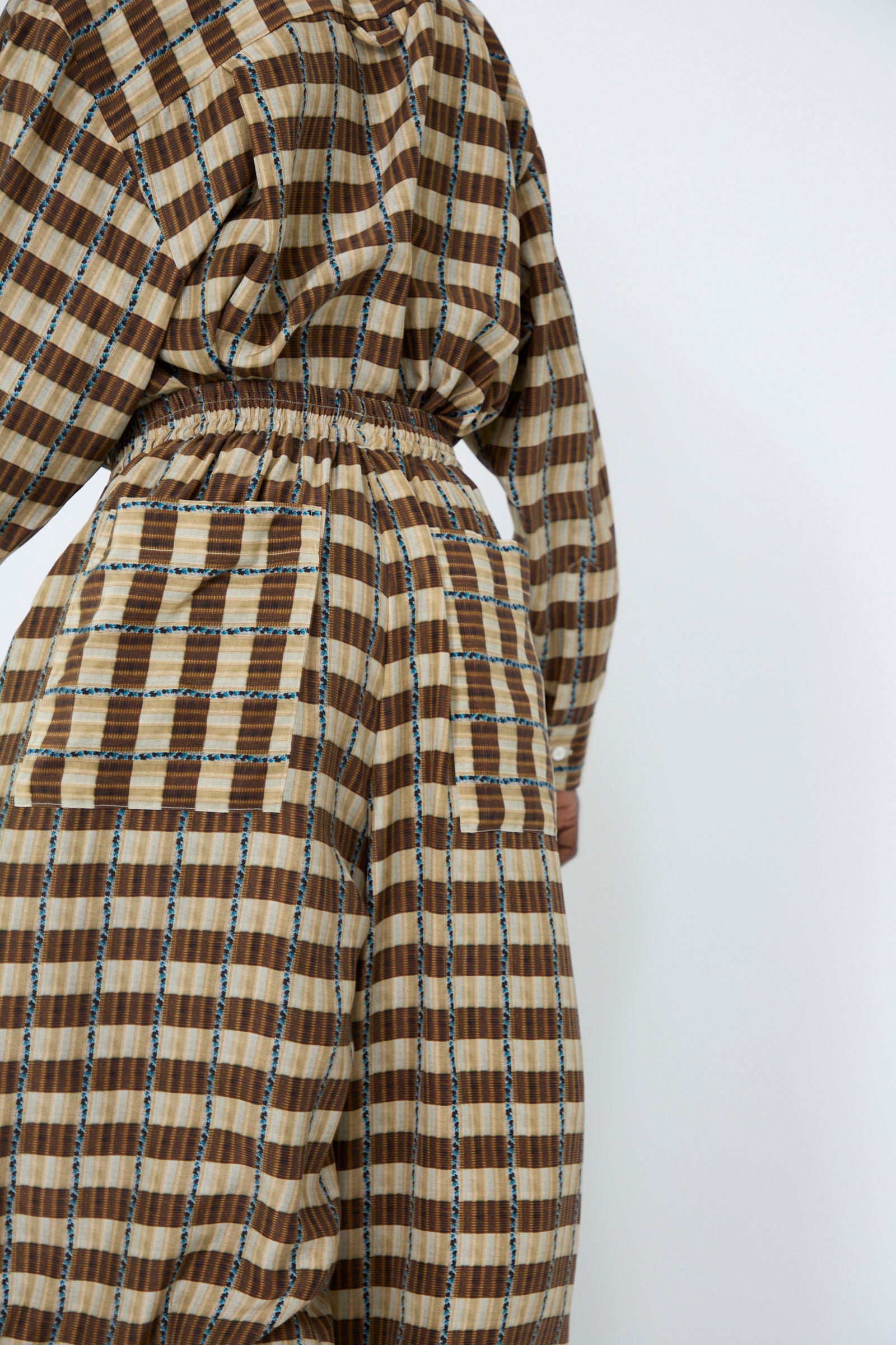 The back of a woman dressed in the Silk Printed May Trouser in Brown Plaid by Cawley, featuring an elasticated waist and two large back pockets.