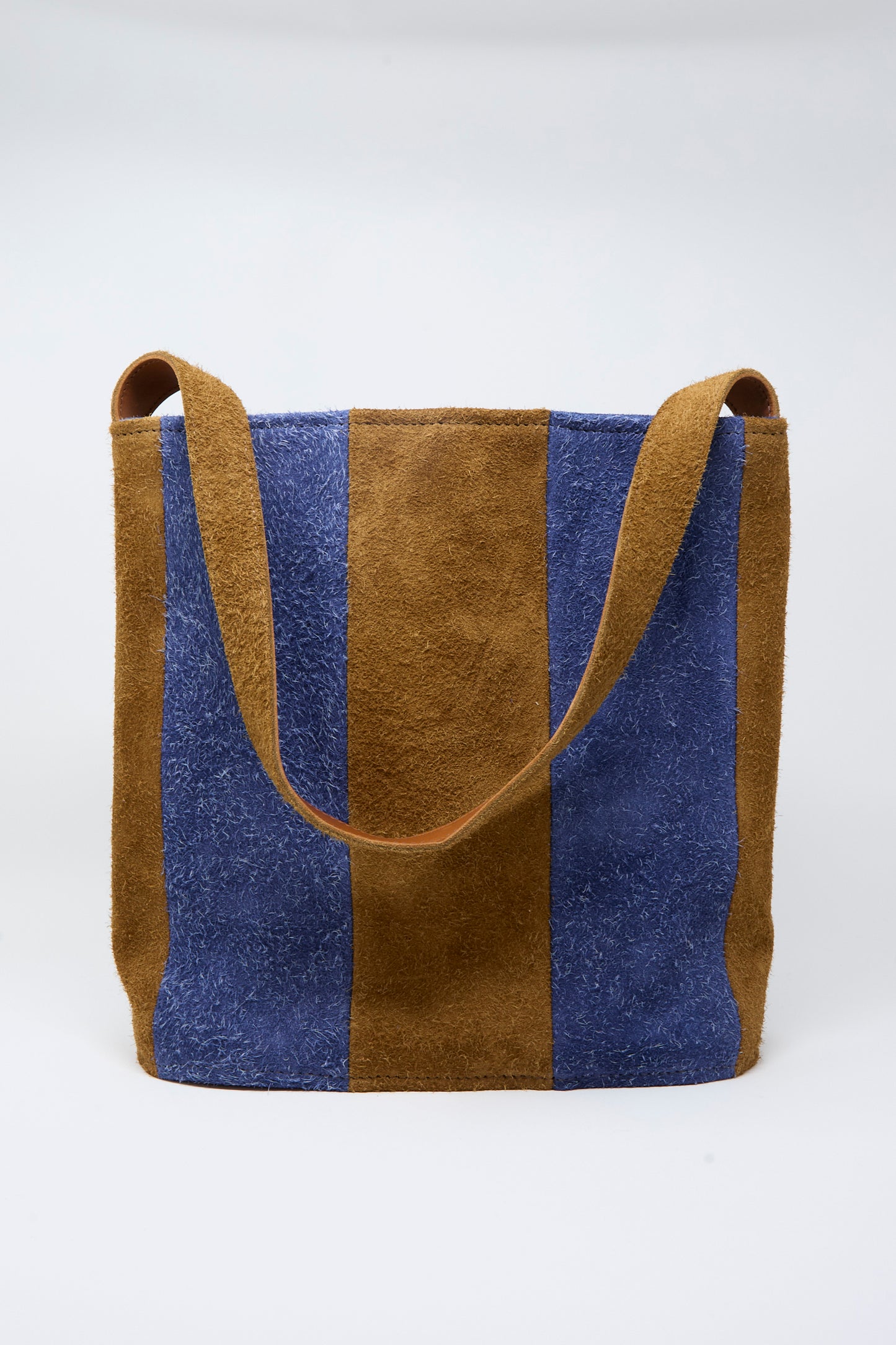 The Cawley Suede Striped Shoulder Bag in Navy and Light Brown features alternating vertical panels of blue and brown suede and a wide shoulder strap, showcased against a plain white background.