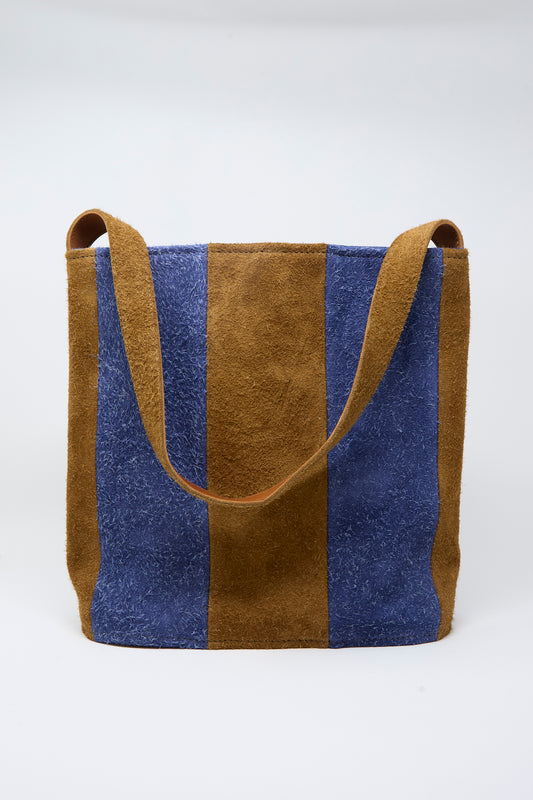 The Cawley Suede Striped Shoulder Bag in Navy and Light Brown features alternating vertical panels of blue and brown suede and a wide shoulder strap, showcased against a plain white background.