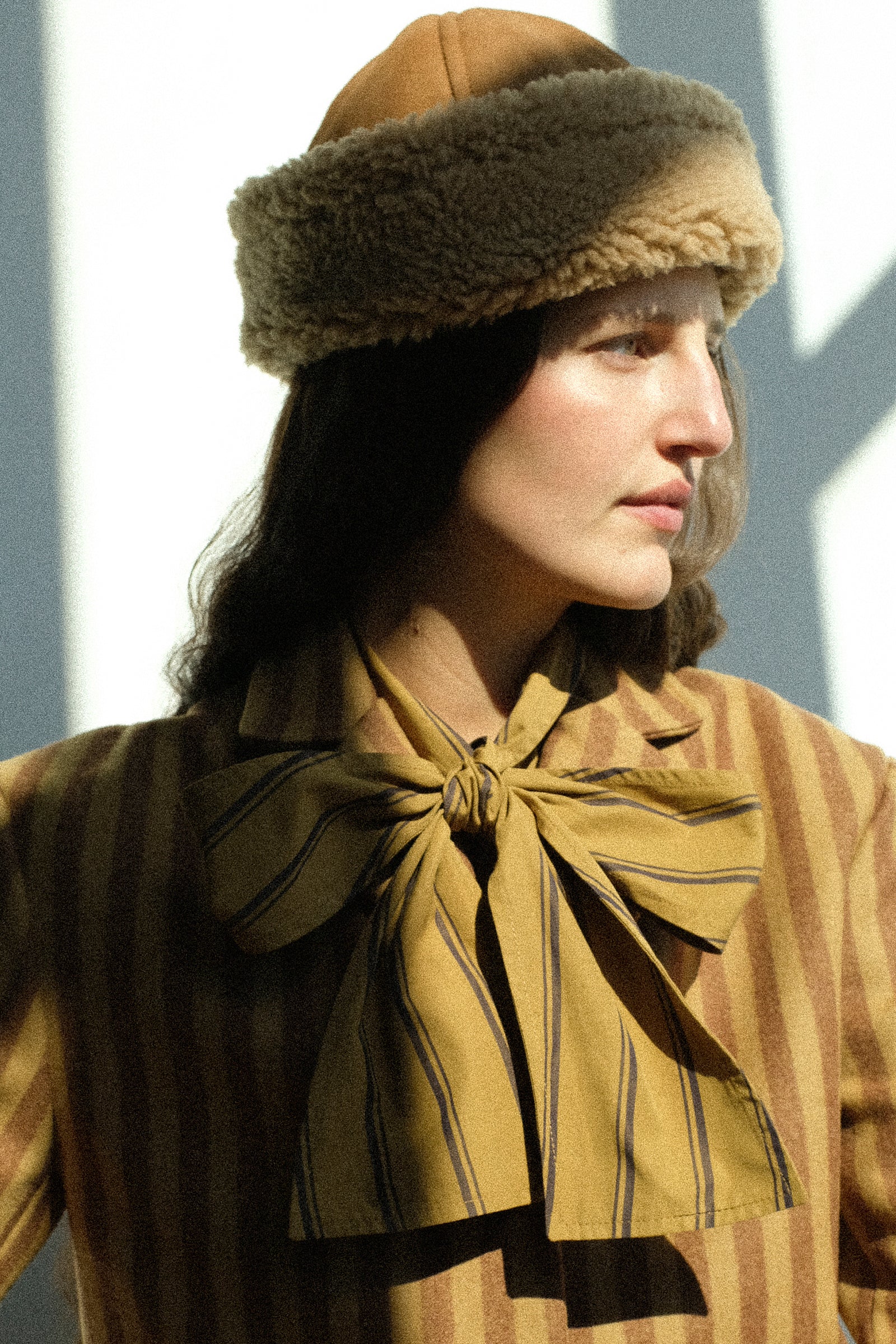 Person wearing Cawley's Suede Back Curly Sheepskin Cap in Tan against a white background.