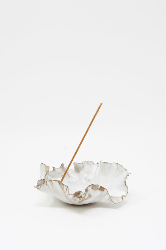 The Wild Petal Incense Holder by Chala Toprak is a white, ruffled stoneware piece featuring a single incense stick placed upright in its center, displayed against a plain white background.