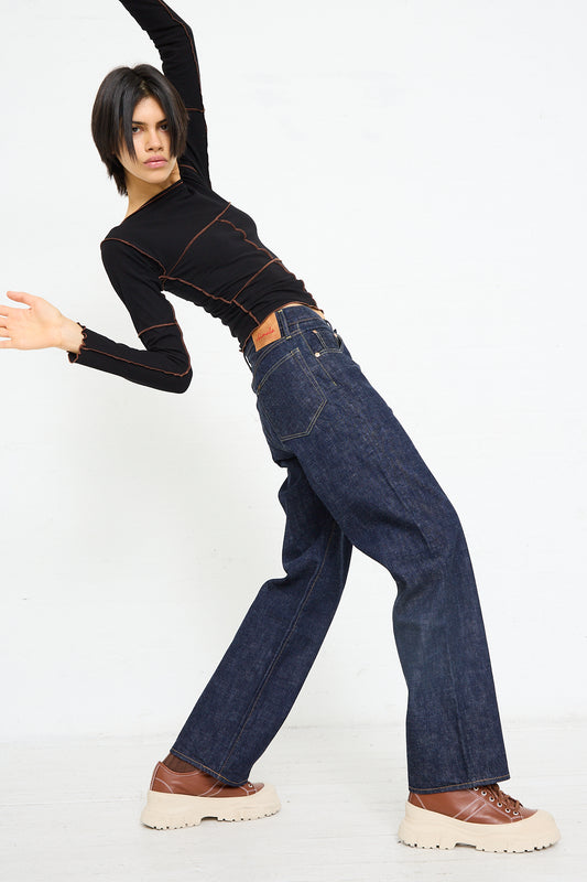 Woman posing in black top and Chimala 13.5 oz. Selvedge Denim Straight Cut in Rinse jeans made of Japanese selvedge denim against a white background.